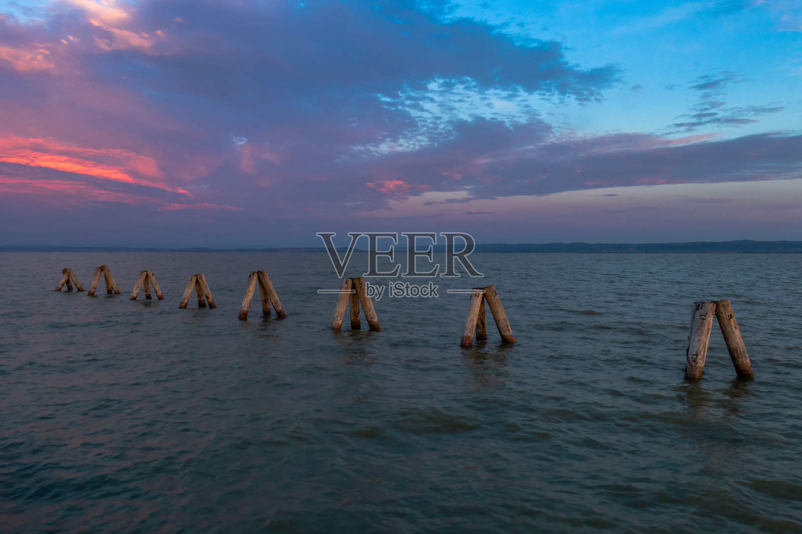奥地利波德斯多夫的Neusiedl湖上，木杆就像防波堤一样。背景是日出时壮观的天空。照片摄影图片