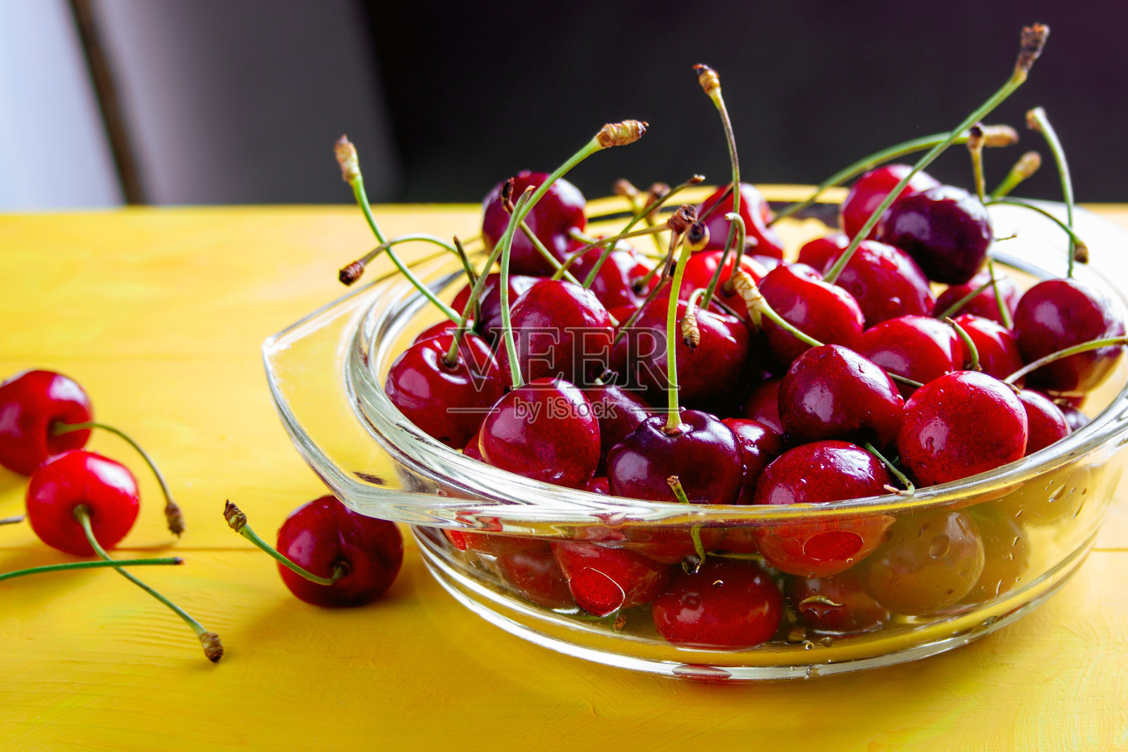 成熟的樱桃浆果装在玻璃碗里，放在黄色的桌子上，夏日的美味照片摄影图片