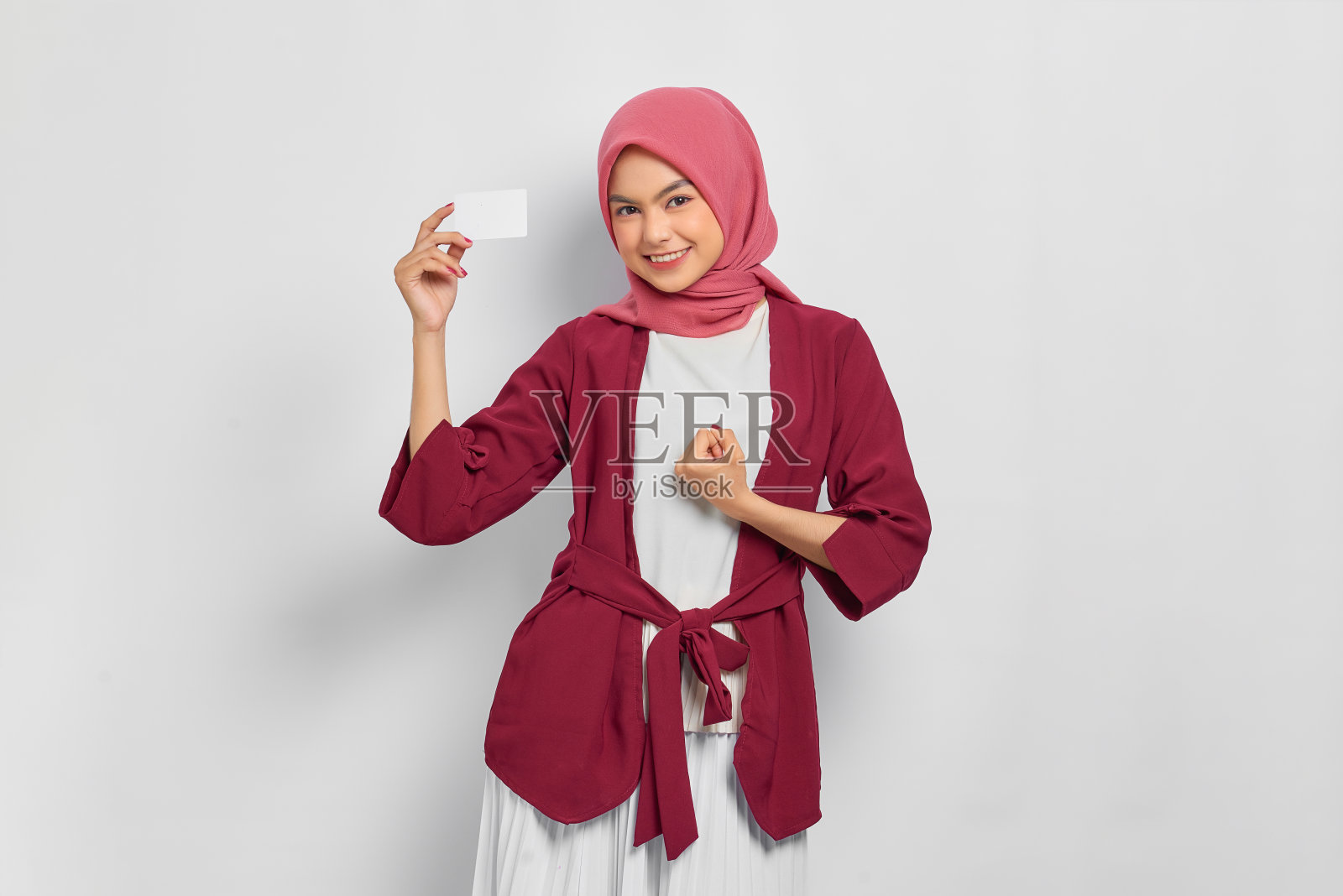 穿着休闲衬衫和希贾布的亚洲美女兴奋地出示信用卡，庆祝与白人背景隔离的胜利。人们的宗教生活方式观念照片摄影图片