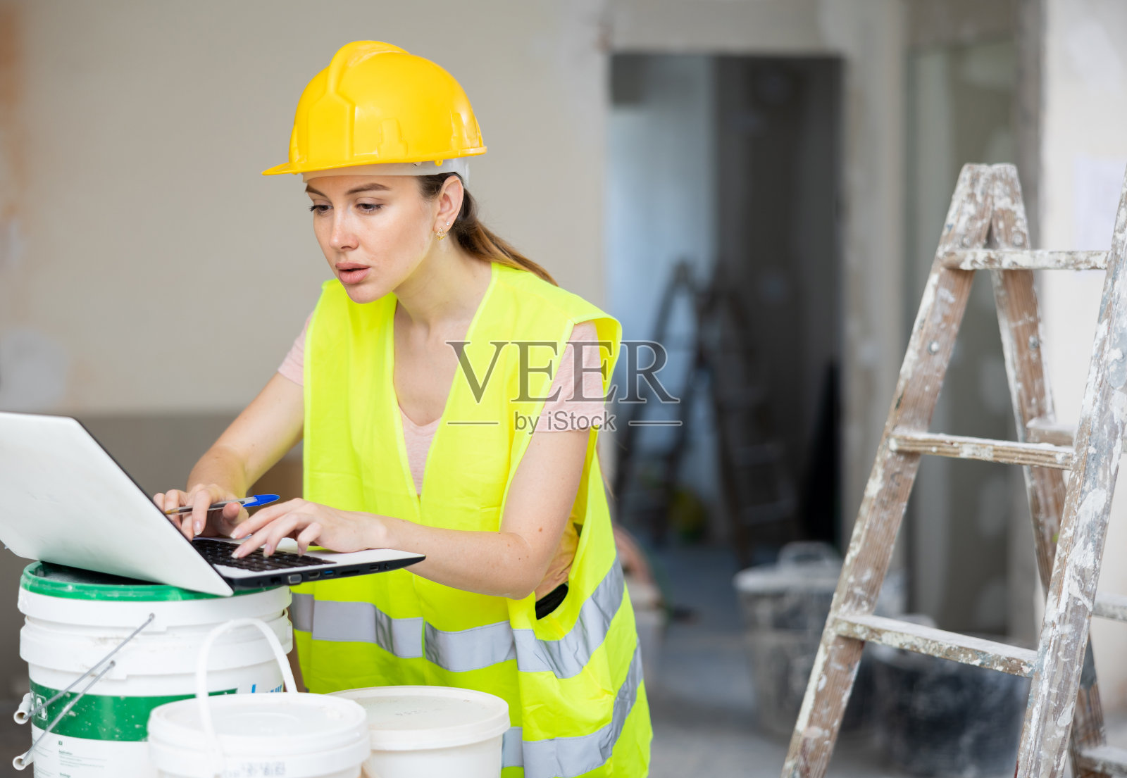 身穿黄色背心、头戴防护帽的女领班使用手提电脑检查维修工作的执行情况照片摄影图片