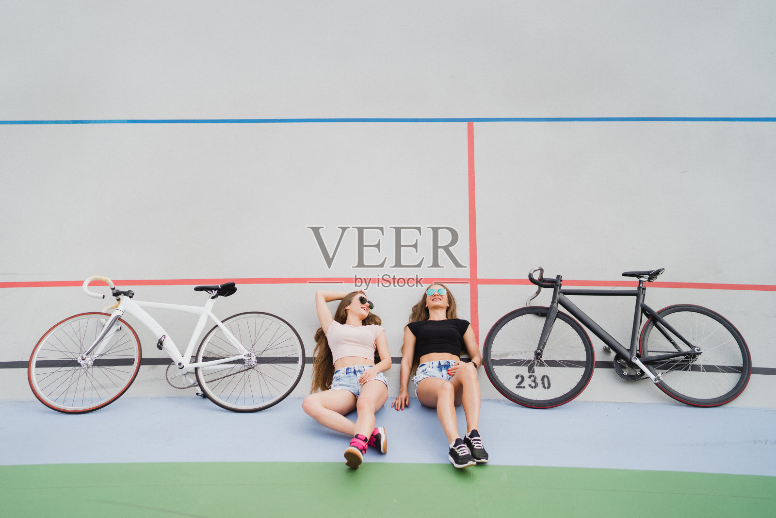 骑自行车和健身。年轻、漂亮、身材完美、穿着运动服的女性在跑道上的户外自行车旁。照片摄影图片