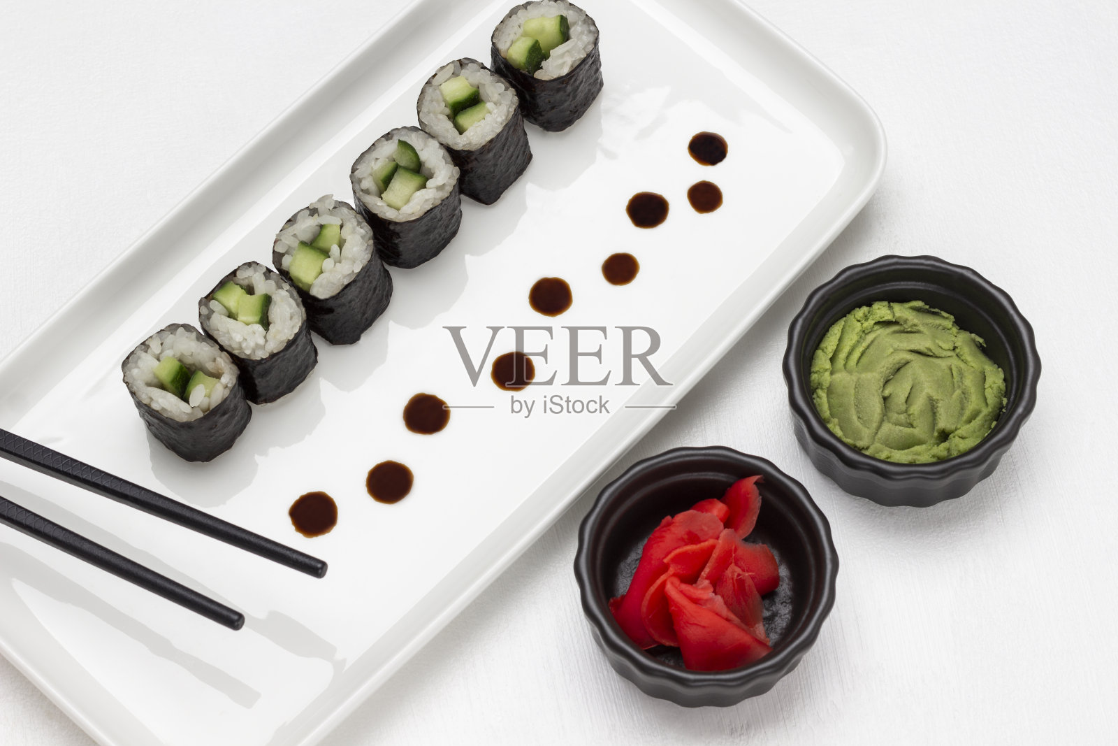 海苔寿司配黄瓜和黑色筷子放在白色盘子上。照片摄影图片