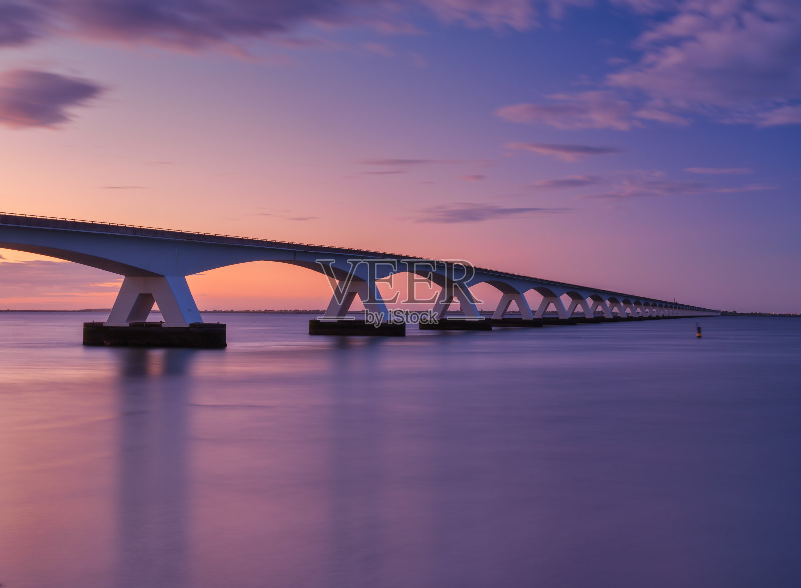 日落时海上的一座长桥。长时间曝光的照片。明亮的日落期间的风景。大海和桥。Zeeland桥,荷兰。照片摄影图片
