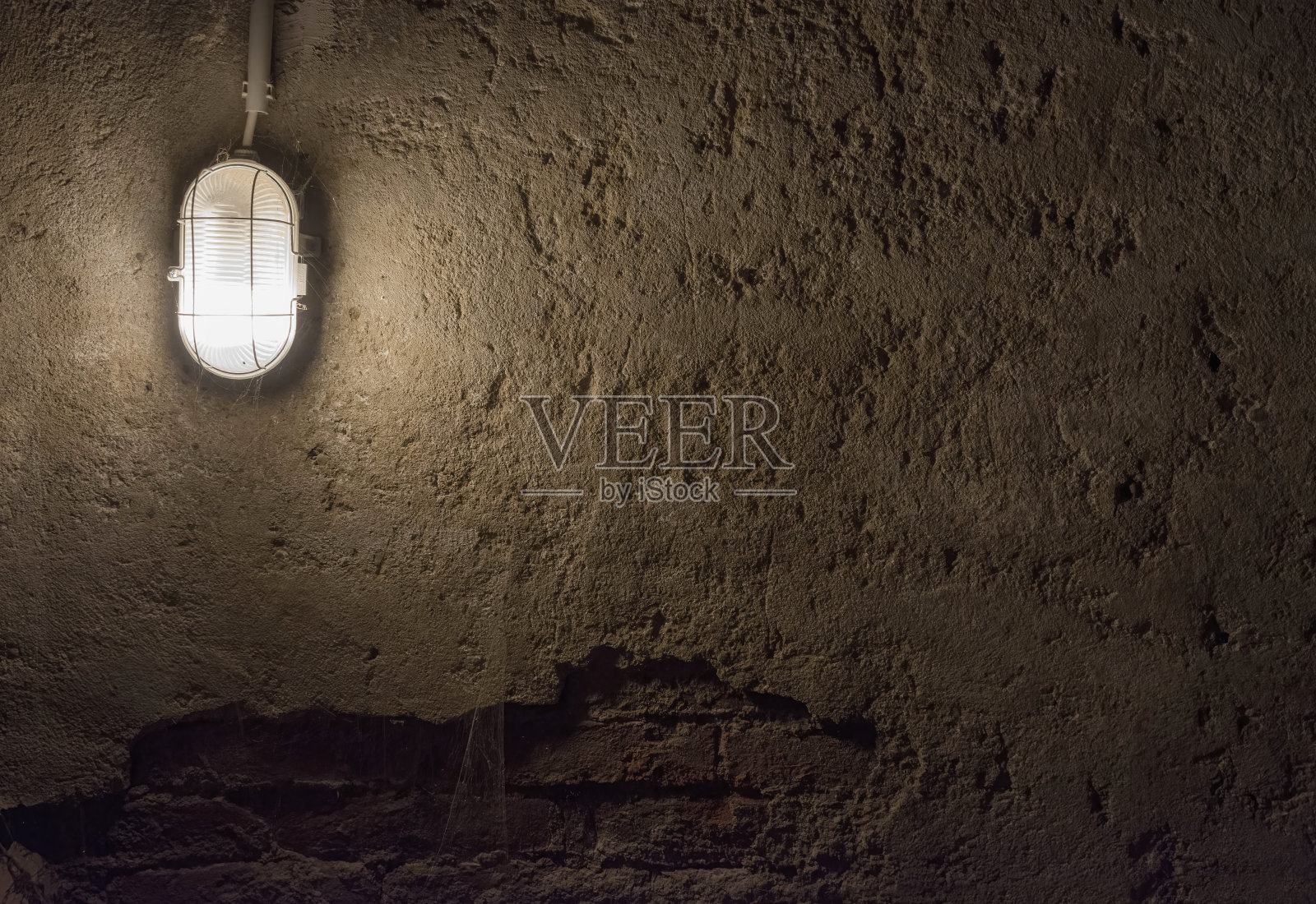 混凝土墙下的工业老吊灯。古老的地下室内部，肮脏的城市地下背景。照片摄影图片