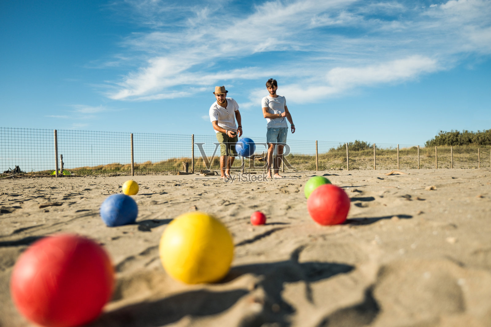 游客们在海边的沙滩上玩一种活跃的游戏——一群年轻人在海滩假日的户外玩球——地上的球照片摄影图片