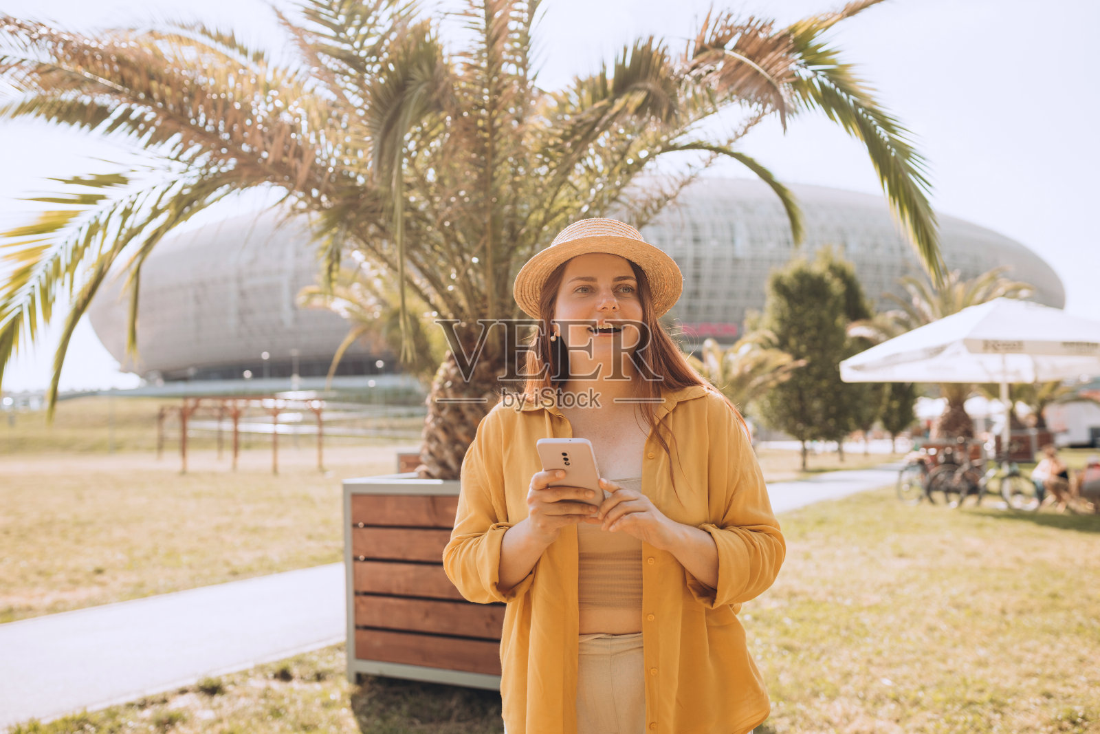 漂亮的笑女孩和智能手机有一个好时光在夏天的周末。棕色头发的时髦女士戴着草帽在户外打电话。电话沟通。城市生活方式的概念。旅行者照片摄影图片
