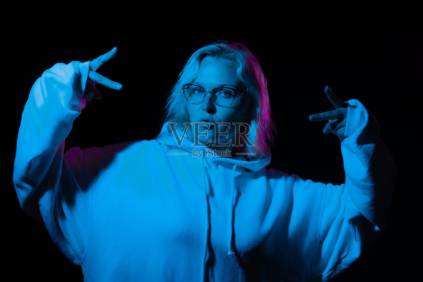 很酷的时髦女人戴着眼镜，在蓝色的光在黑色的背景上的卫衣照片摄影图片