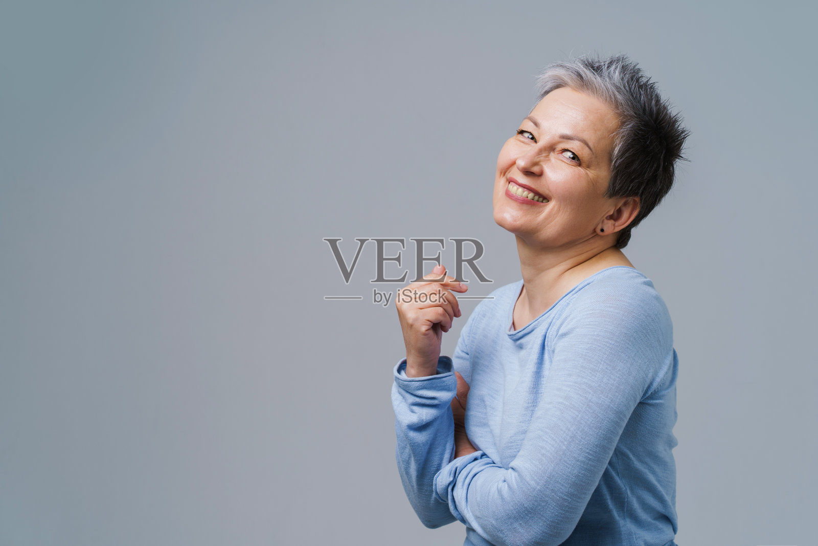 积极的情绪成熟的灰色头发的女人摆着双手合十看着相机穿蓝色衬衫，复制空间在左边孤立的白色背景。保健、老年美容理念照片摄影图片
