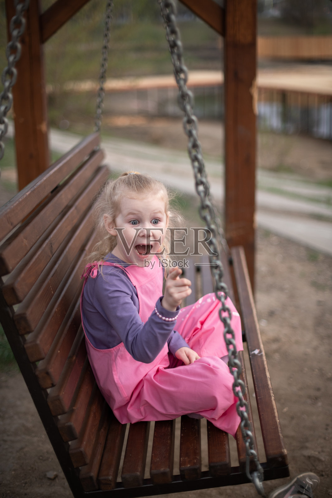 一个金发女孩在花园里跷着腿坐在秋千上。照片摄影图片