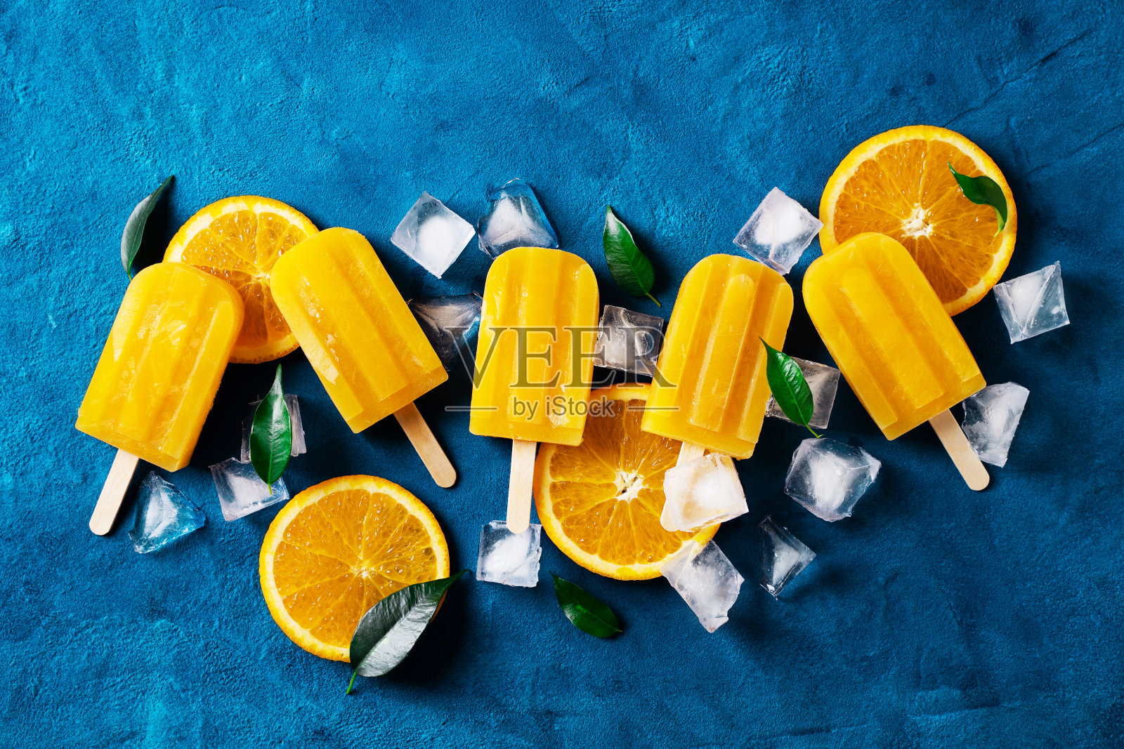 冰淇淋棒冰橙色与冰块和绿色叶子在蓝色的背景照片摄影图片