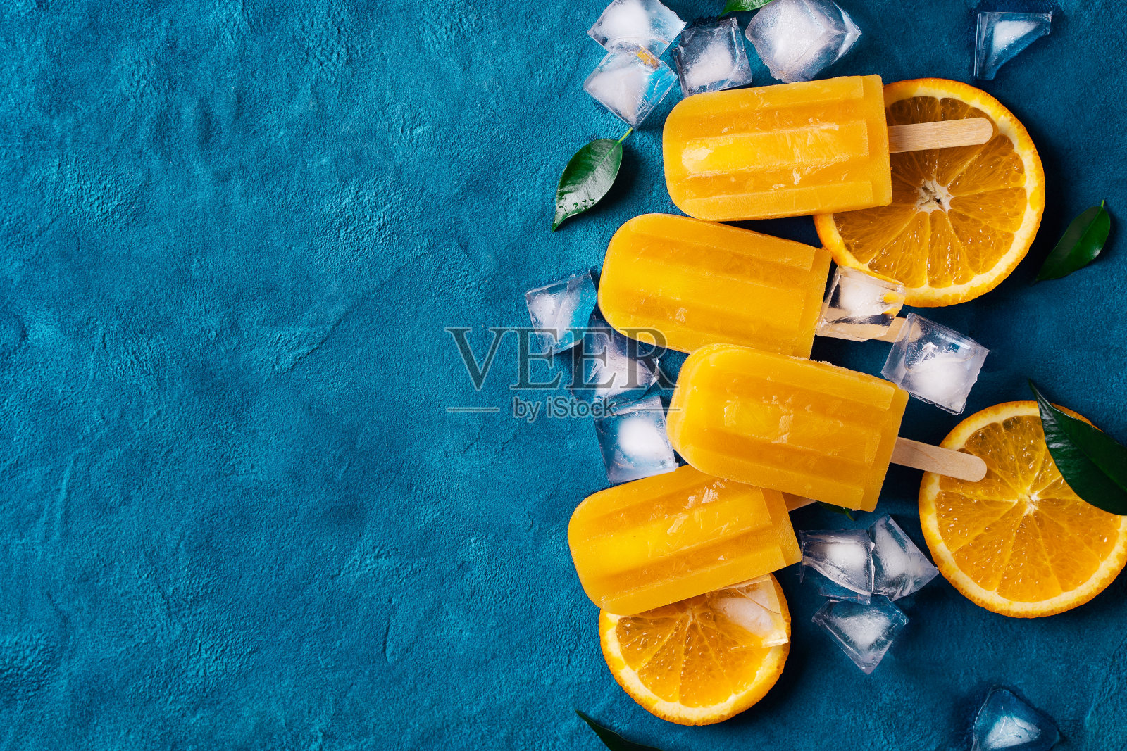 冰淇淋棒冰橙色与冰块和绿色叶子在蓝色的背景照片摄影图片