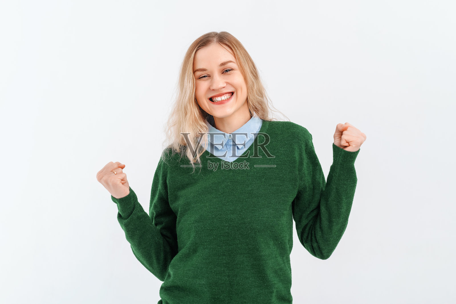 热情的年轻女子赢了，举起拳头庆祝，高兴地喊着，穿着休闲的衣服。室内工作室拍摄的白色背景照片摄影图片