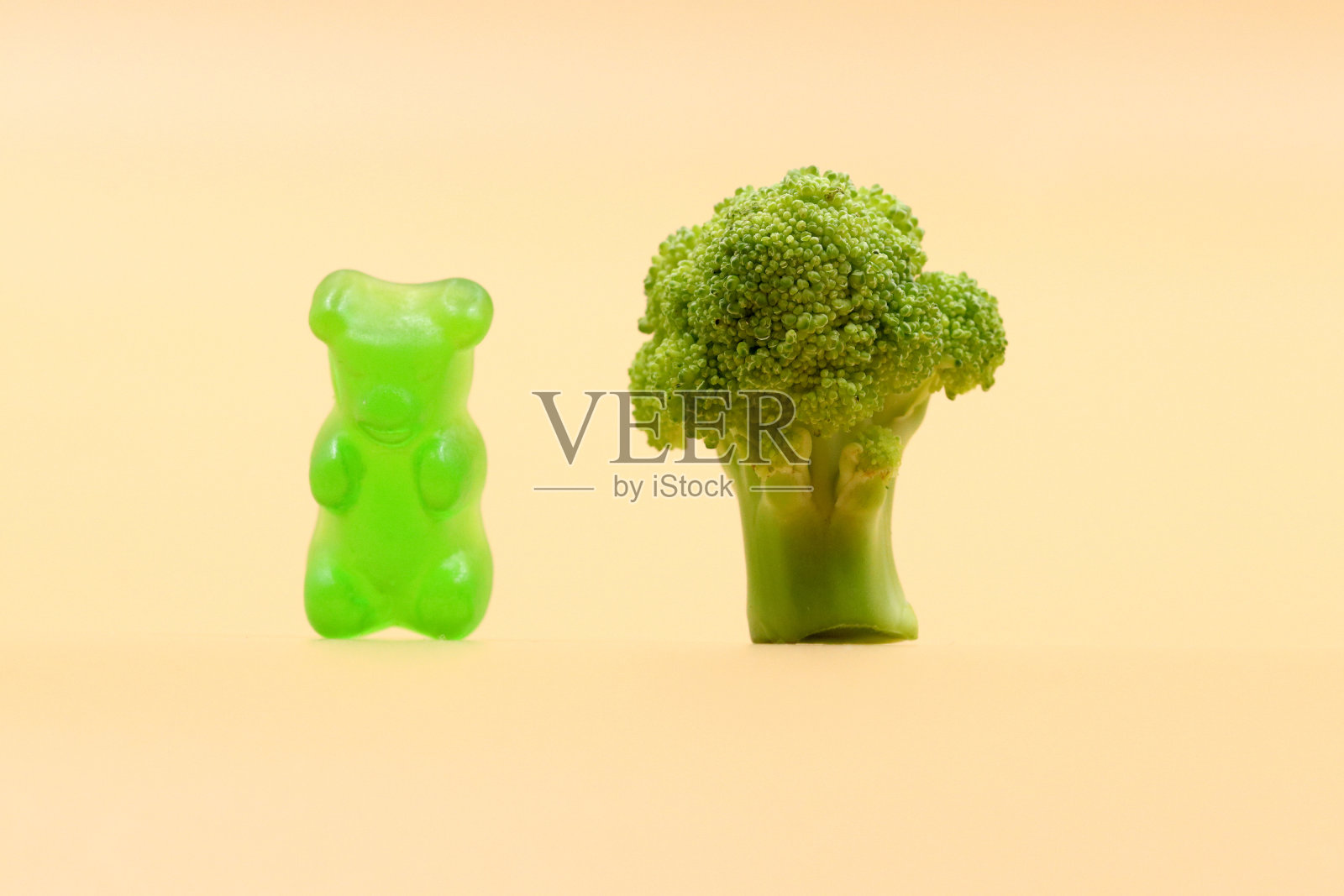 不良和健康食品的概念。一根花椰菜旁的小熊软糖。照片摄影图片