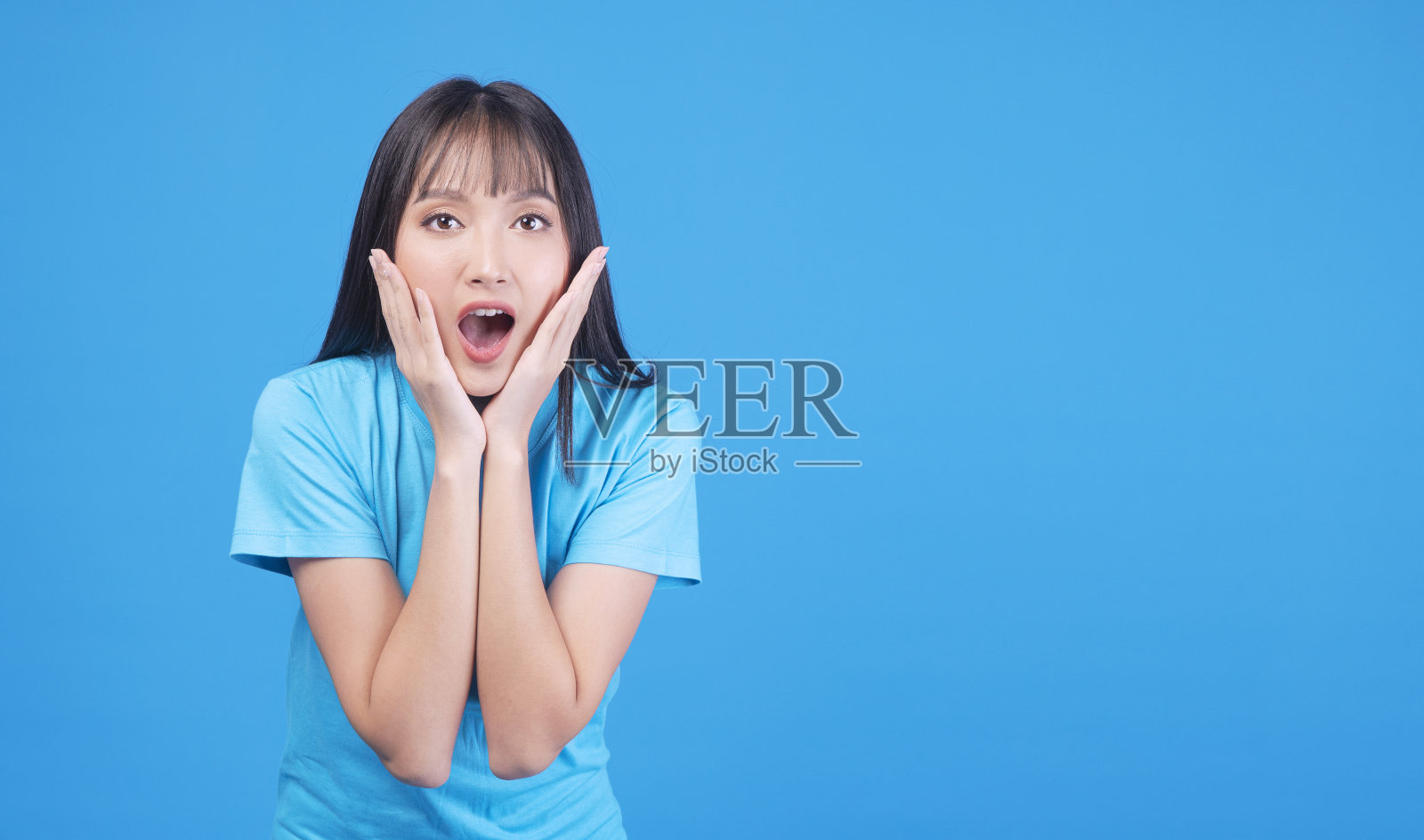 激动的亚洲妇女手在嘴震惊惊讶销售产品的拷贝空间在蓝色的背景。开朗的小女孩情绪激动，惊讶地尖叫着哇哇什么就孤立了。购物的概念照片摄影图片