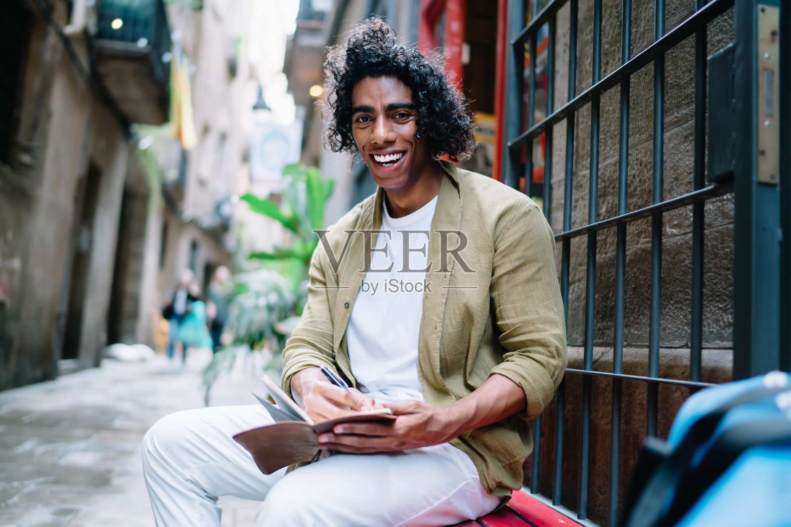 欢快英俊的卷毛男士穿着休闲服装，闲暇时在户外画画，微笑的20多岁的年轻潮男在创作文章，满足于老城的休闲照片摄影图片
