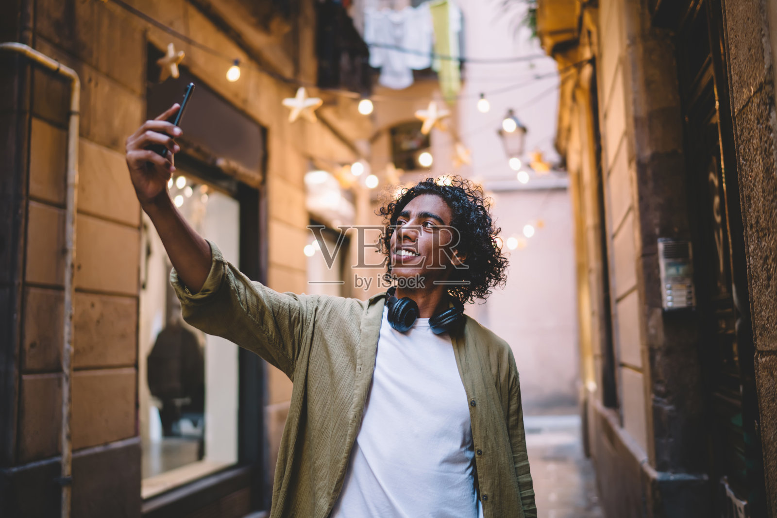 穿着时髦休闲装的帅气白人男子在城市历史中心用智能手机自拍，积极的卷毛男博主用手机拍摄视频分享照片摄影图片