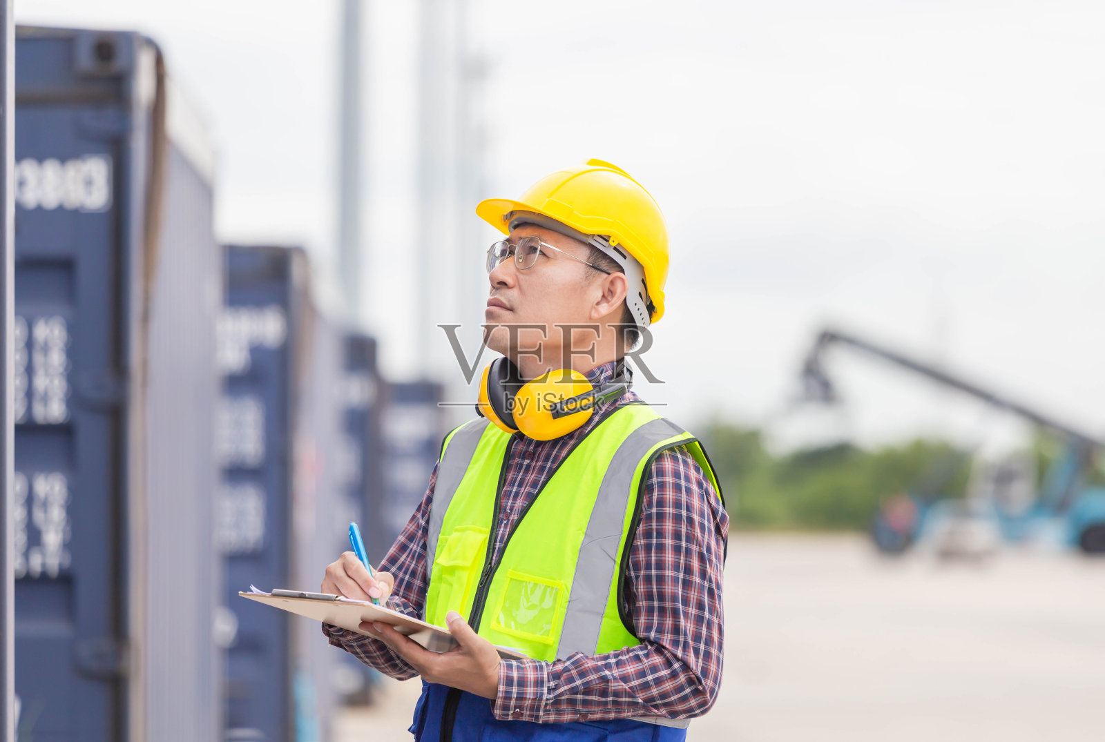 领班戴安全帽，穿着安全背心控制集装箱货物的装卸，工程师用写字板检查，工业工人装卸工业集装箱货物照片摄影图片