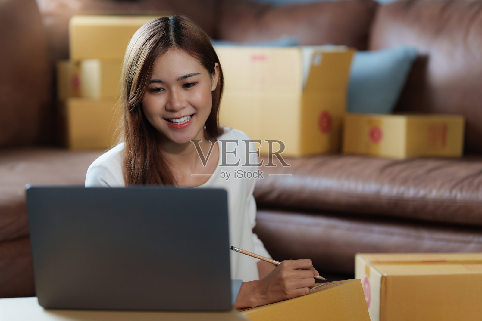 年轻的亚洲女性拿着包裹盒子开始自由职业，用笔记本电脑和顾客交谈。网上营销包装箱配送理念。照片摄影图片