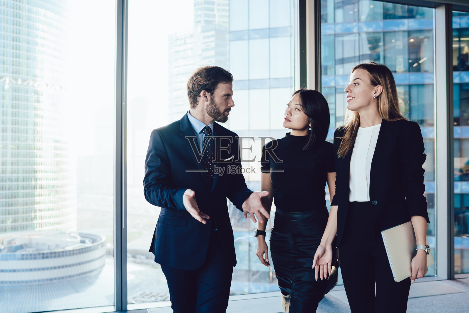 繁华的男老板穿着正装走进办公室内部与女行政助理讨论工作流程，一群女同事和男同事互相谈论业务照片摄影图片