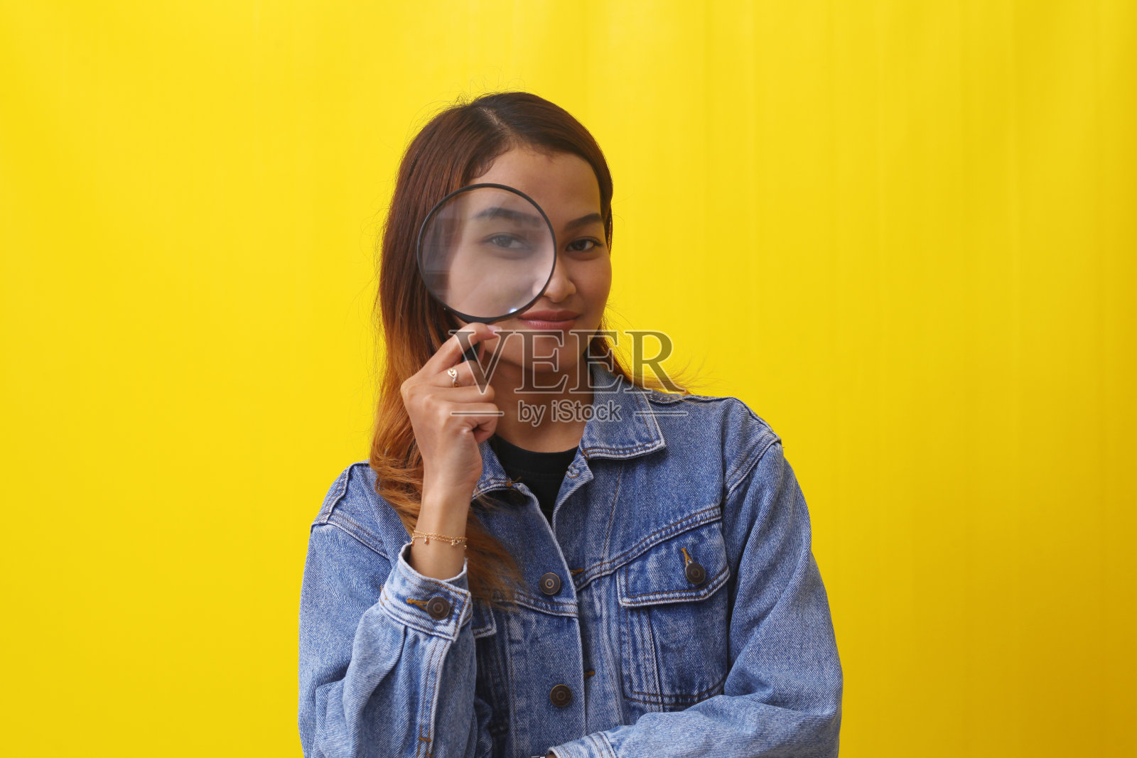 微笑的亚洲女人站在一边通过放大镜看。孤立在黄色背景上照片摄影图片