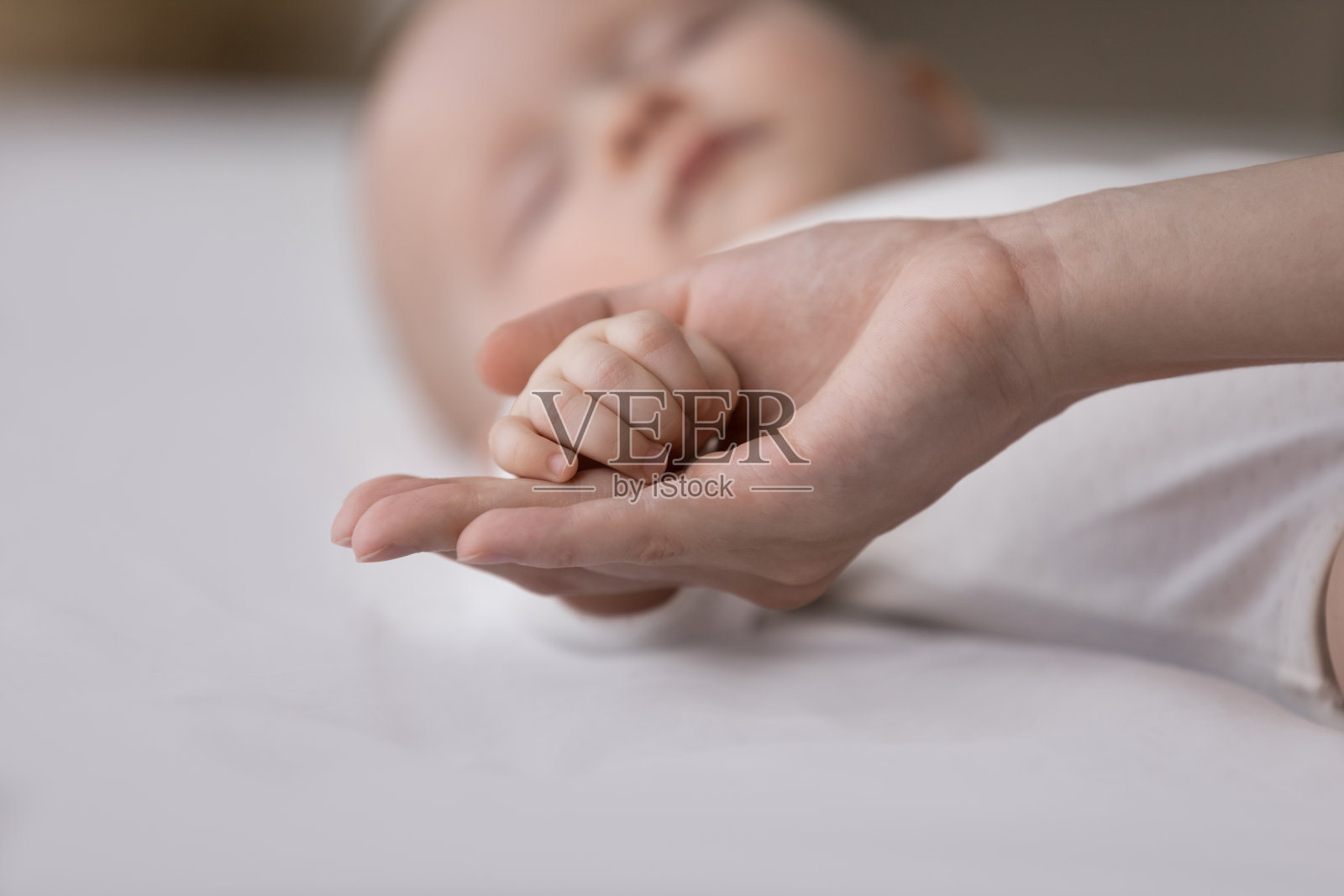 慈爱的母亲紧紧地抱着熟睡的婴儿的小胳膊照片摄影图片