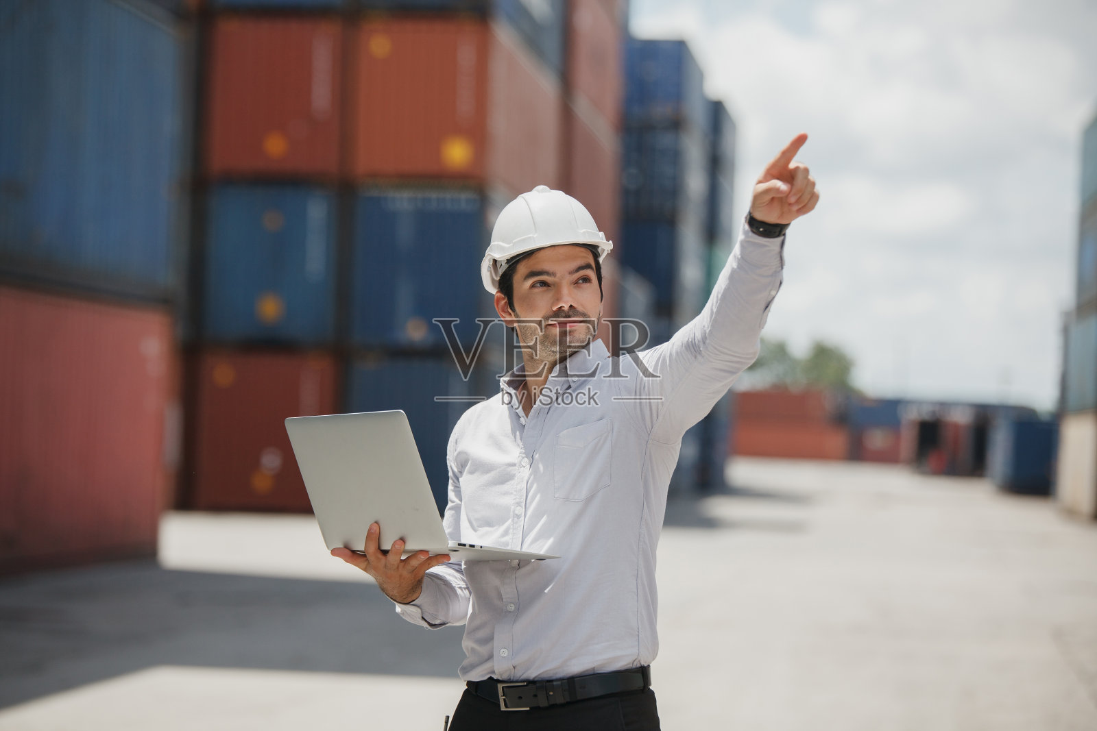 工程师穿着普通的西装，微笑着拿着笔记本电脑站在集装箱堆场。进出口产品。制造运输和全球化的经营理念照片摄影图片