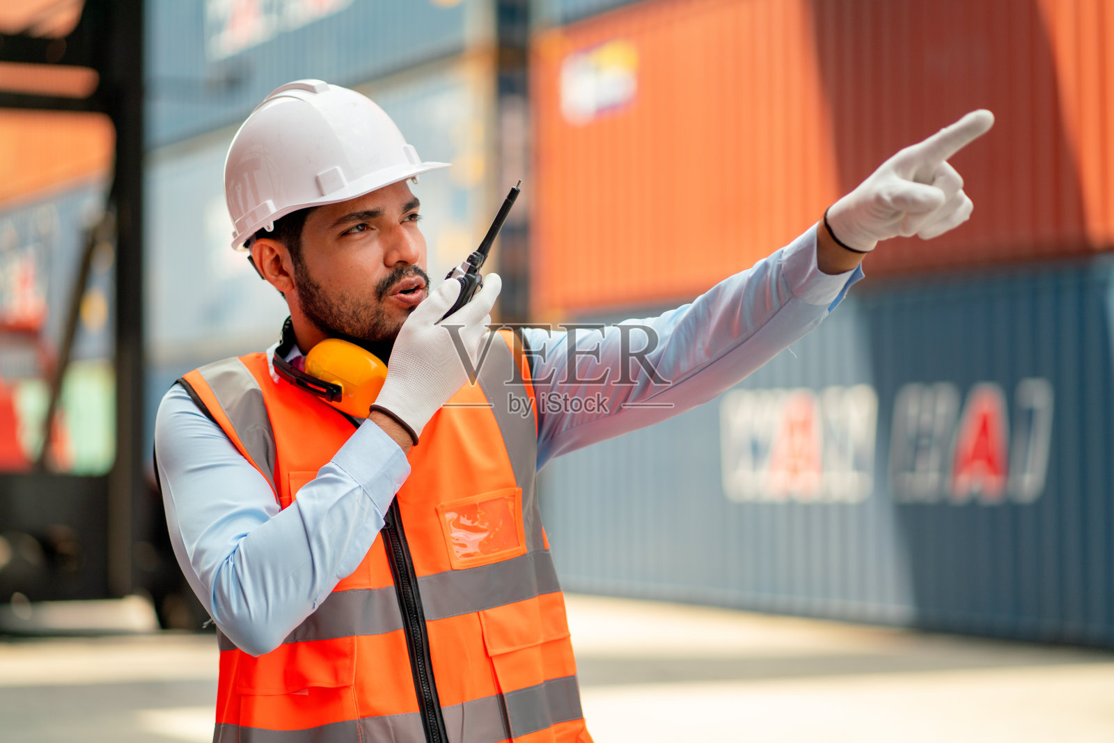 亚洲专业集装箱工人或技术人员在工作场所使用对讲机或无线电与同事联系时也指向右侧。照片摄影图片