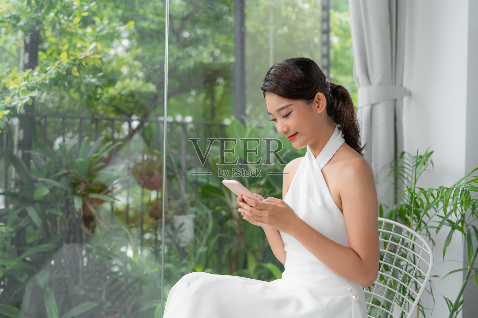 一个微笑快乐的女人的肖像坐在椅子上与手机照片摄影图片