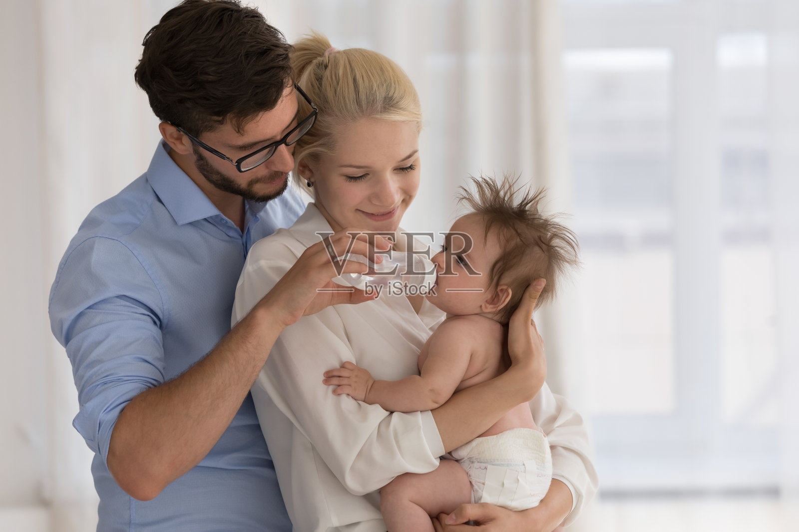 宝宝穿着尿布，抱在父母的怀里，从奶瓶里喝水照片摄影图片