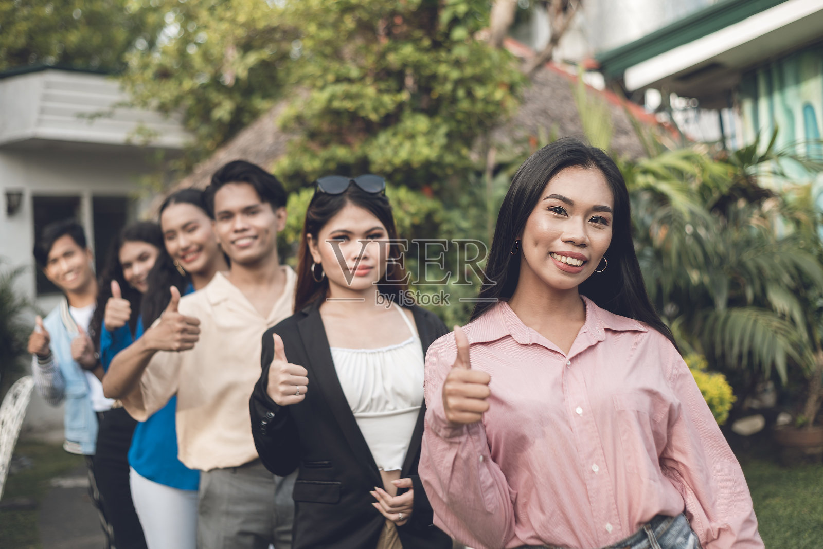 六个年轻而有活力的朋友，从十几岁到二十岁出头，在一个文件中竖起大拇指。室外场景。照片摄影图片