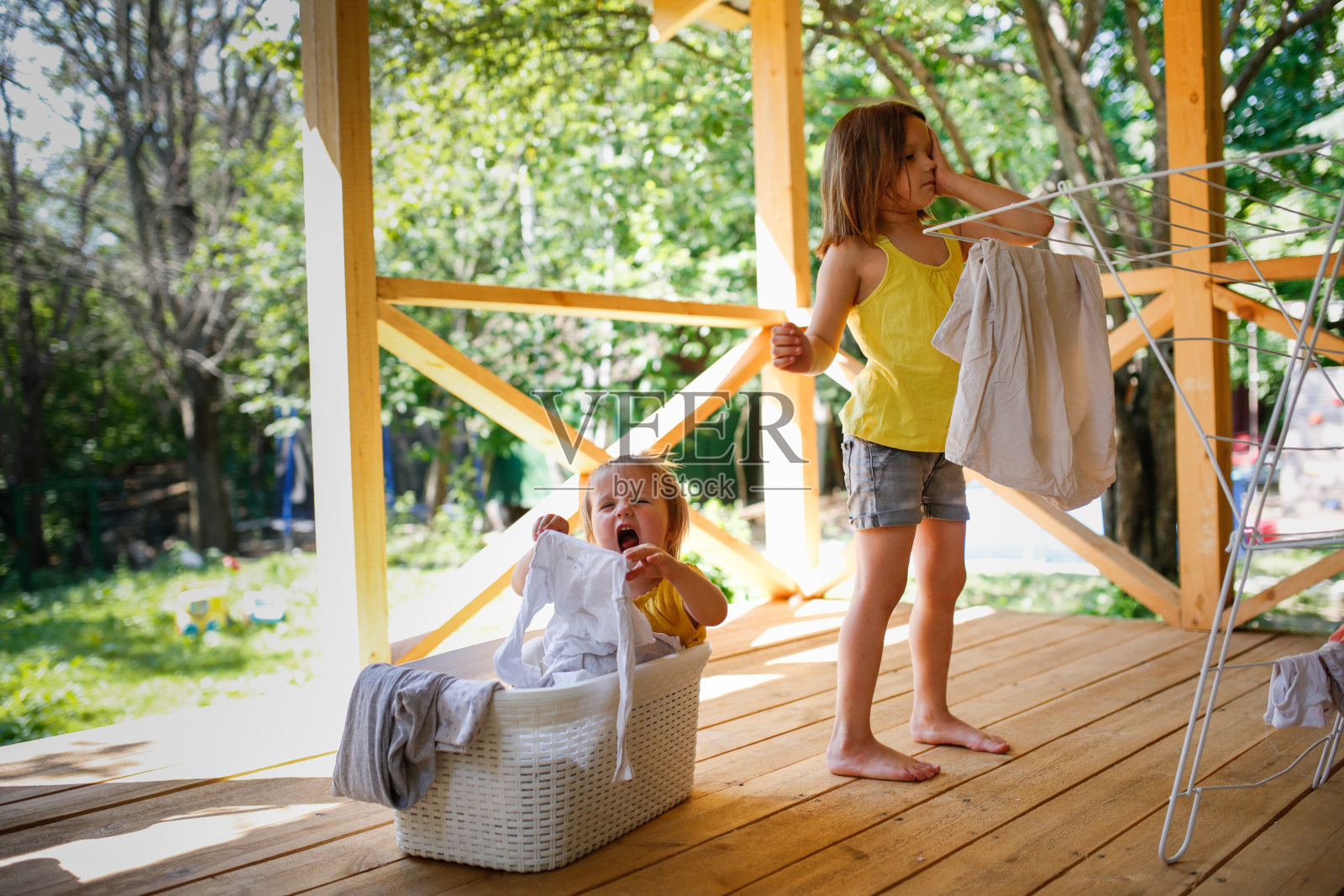 女孩姐妹们帮忙做家务，孩子们把洗好的衣服从塑料篮子里挂在地板烘干机上，在房子附近的后院，夏天照片摄影图片