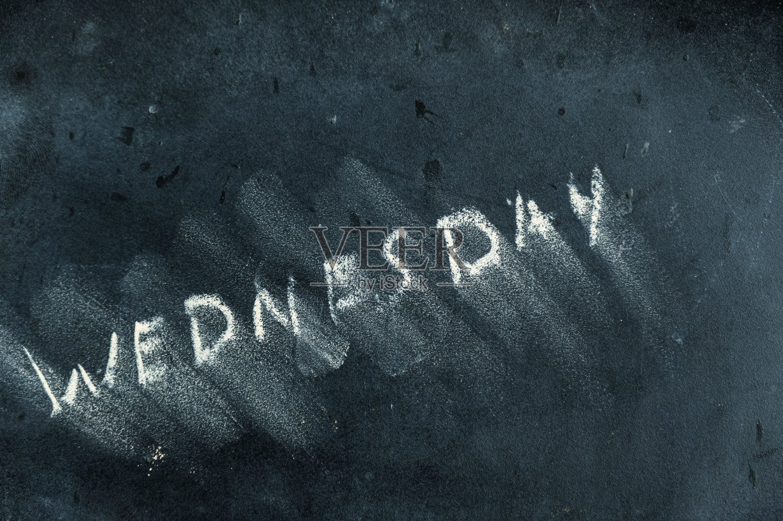 黑色黑板上半抹去的字星期三。手写的字。黑色表面模糊的字母。一周中天数交替的概念。日历照片摄影图片