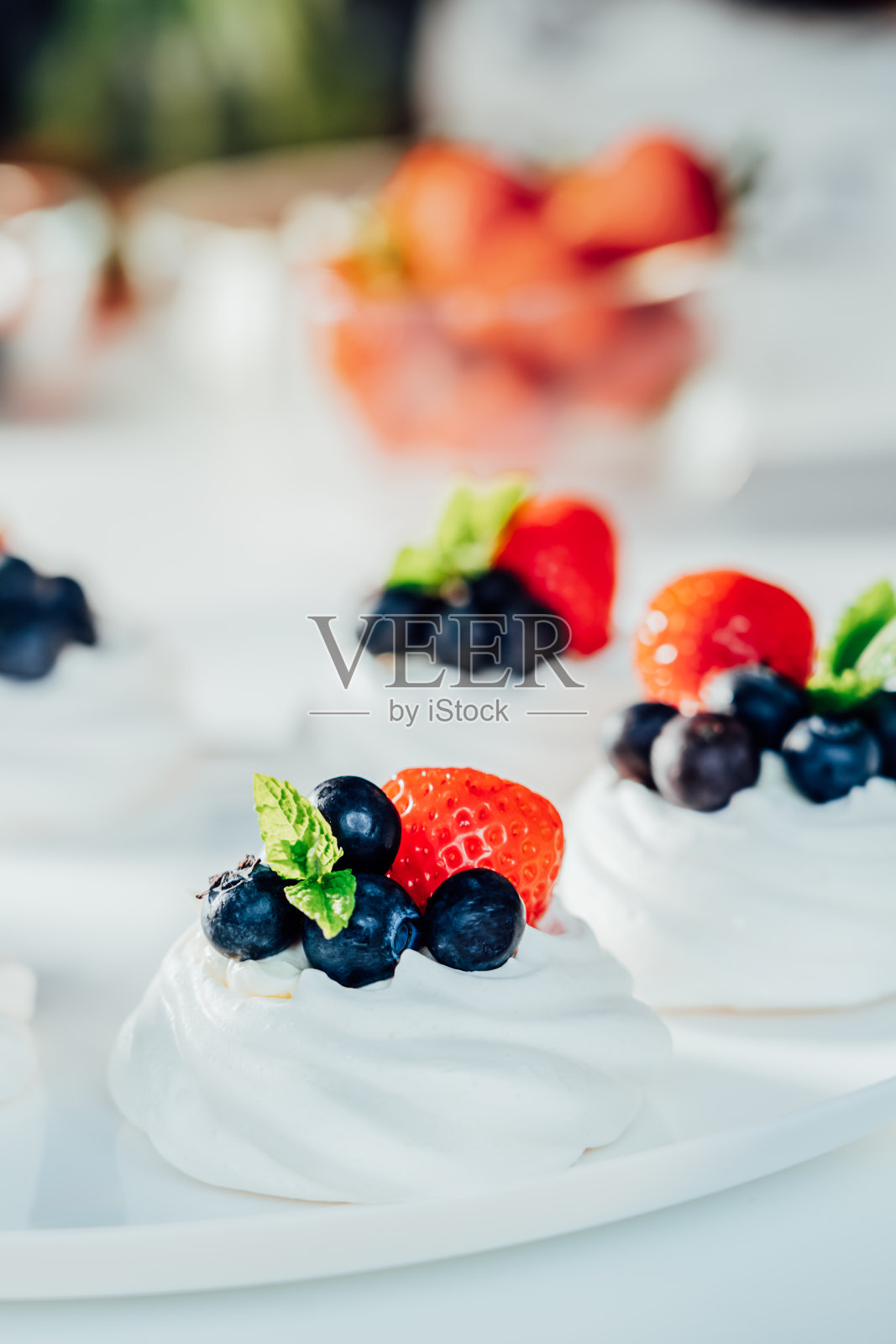 蛋白霜甜点巴甫洛娃蛋糕配上新鲜的奶油、草莓和蓝莓，再用薄荷装饰在白色的盘子上。清淡美味的甜点食谱。糖果咖啡馆菜单。有选择性的重点照片摄影图片