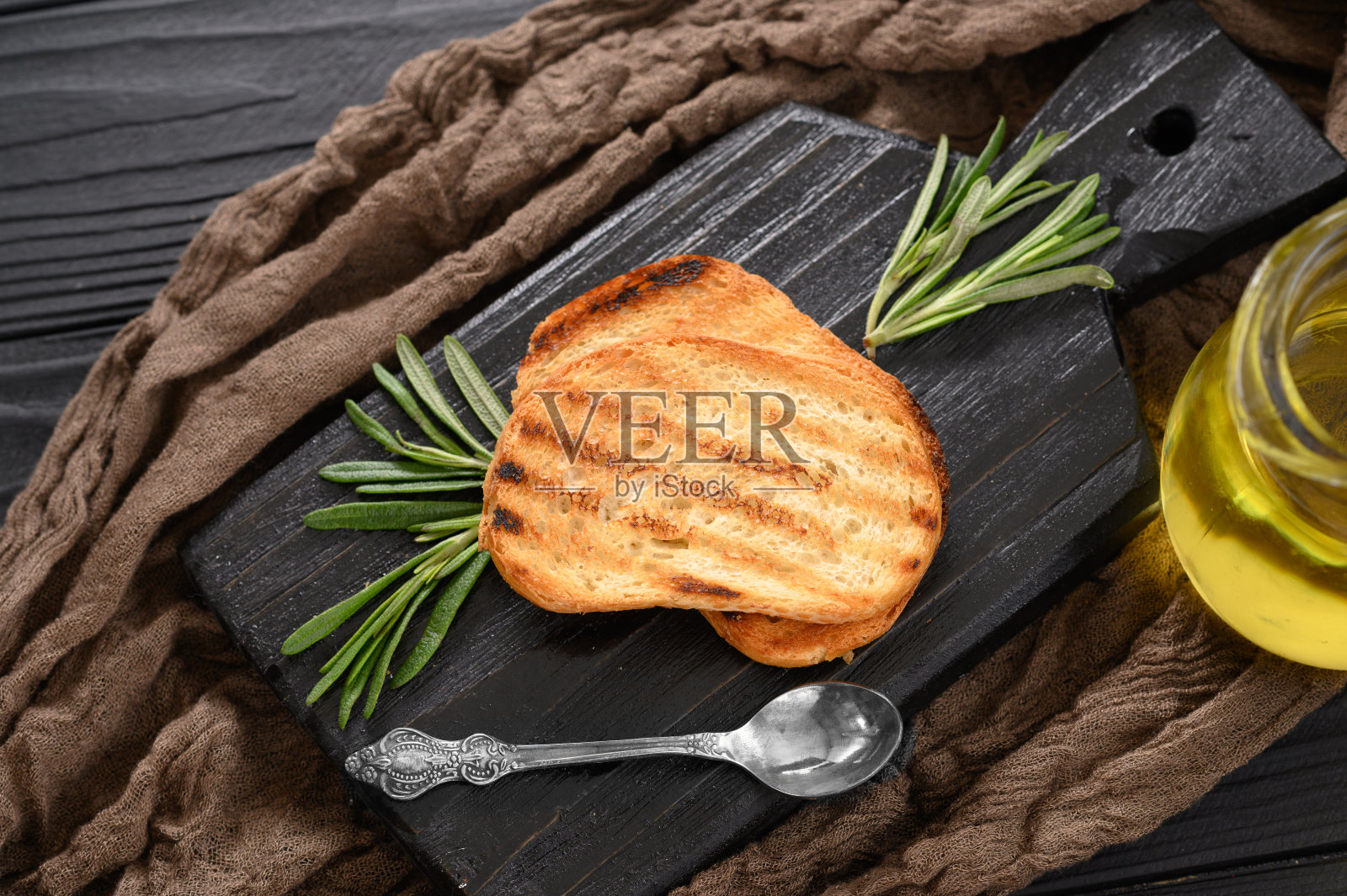 切片烤面包，在黑色的背景上加入特级初榨橄榄油和迷迭香照片摄影图片