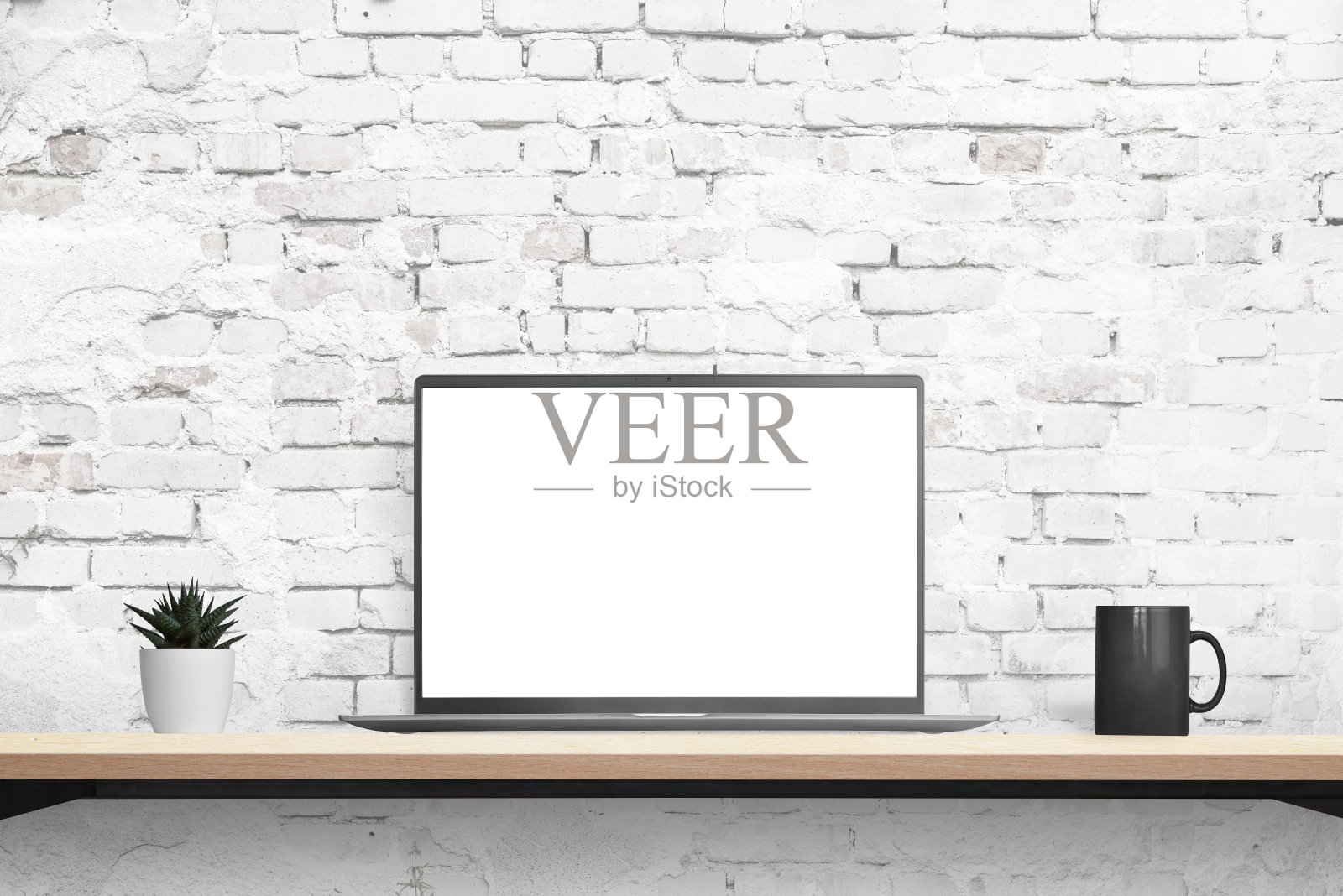 笔记本电脑模型放在桌子上，背景是砖墙。孤立的白色展示模型，应用程序或网页推广。旁边有植物和咖啡杯。前面的位置照片摄影图片