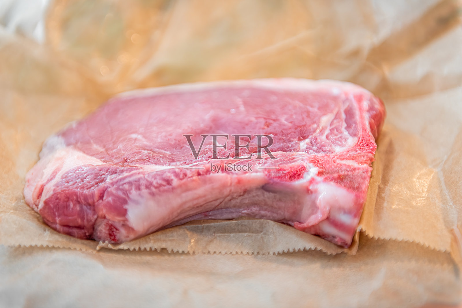 从屠夫手中切下牛皮纸包裹的猪排，红色生肉带骨特写照片摄影图片