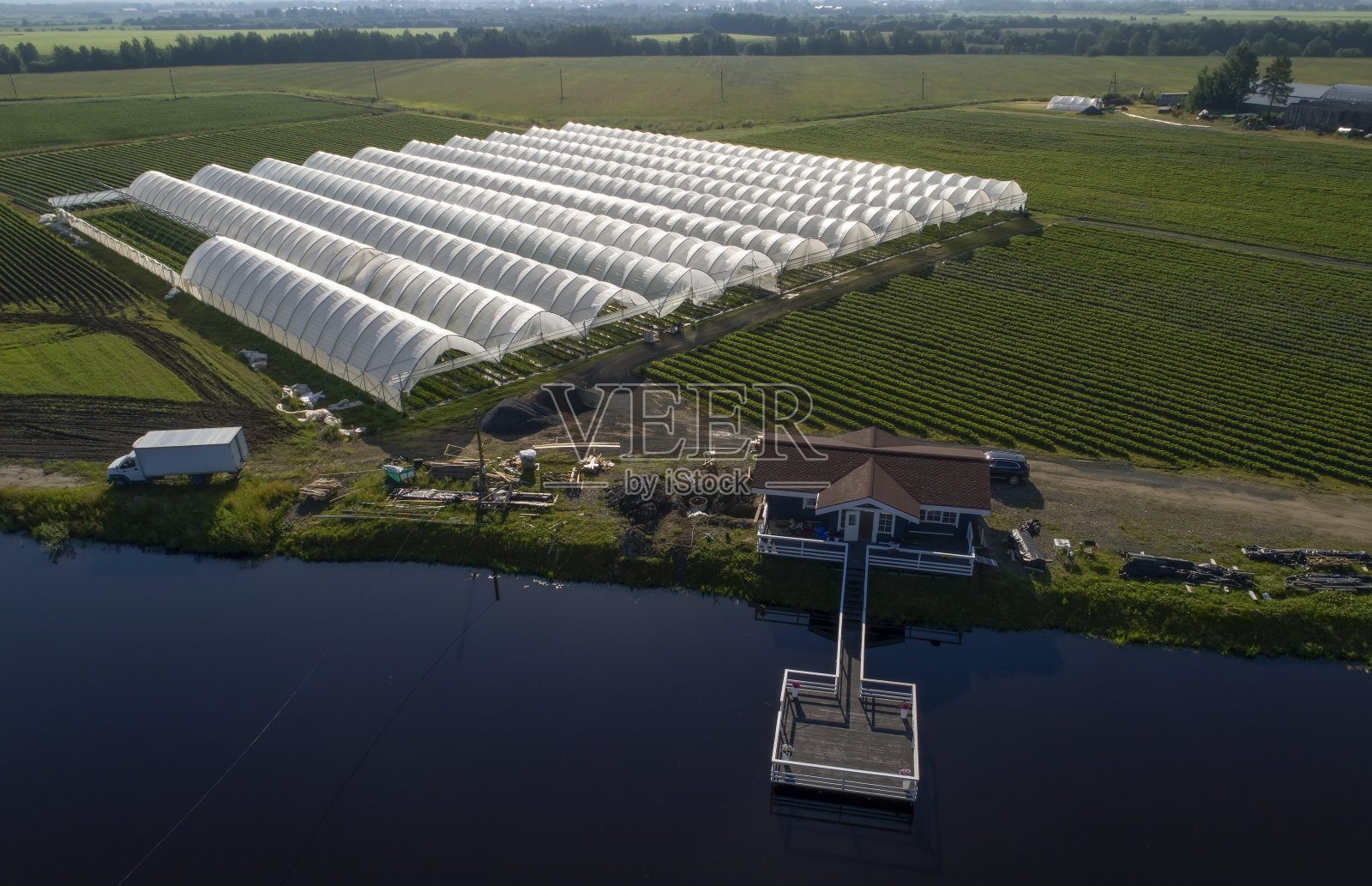 从空中俯瞰，可以看到种植草莓的温室。国家农业。河岸上的木屋。照片摄影图片