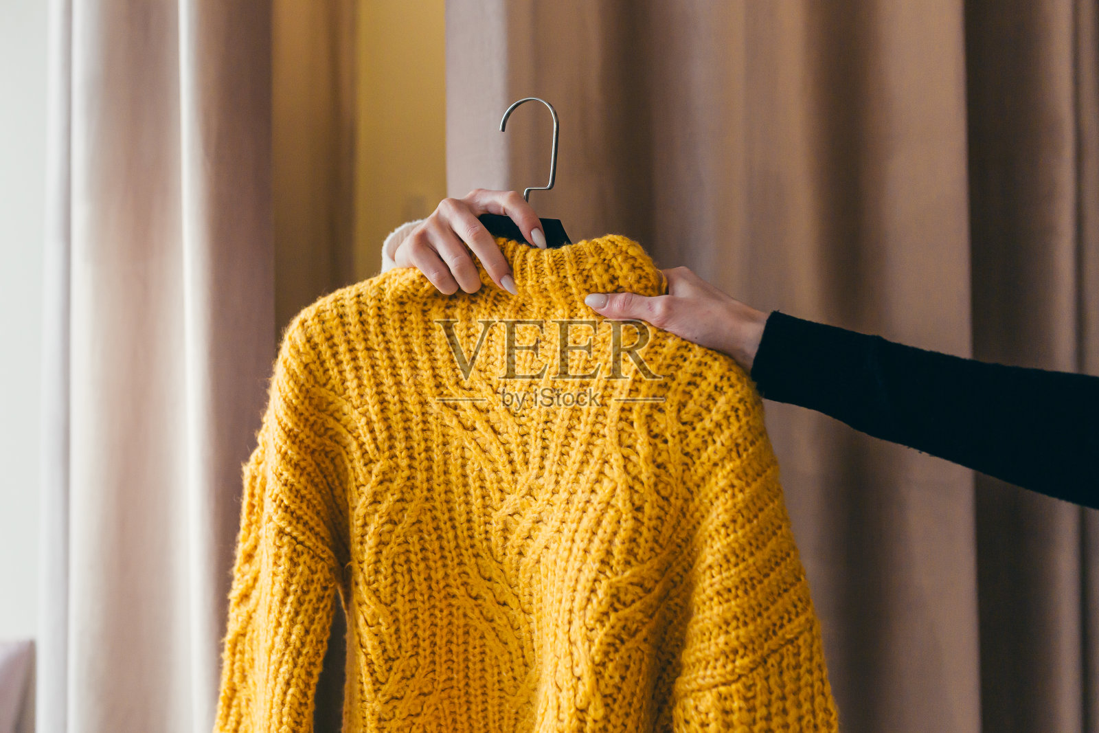 特写照片。销售人员或顾问把挂在衣架上的黄色毛衣递给在窗帘后面试衣间等候的客户的手。在购物中心的一家服装店照片摄影图片