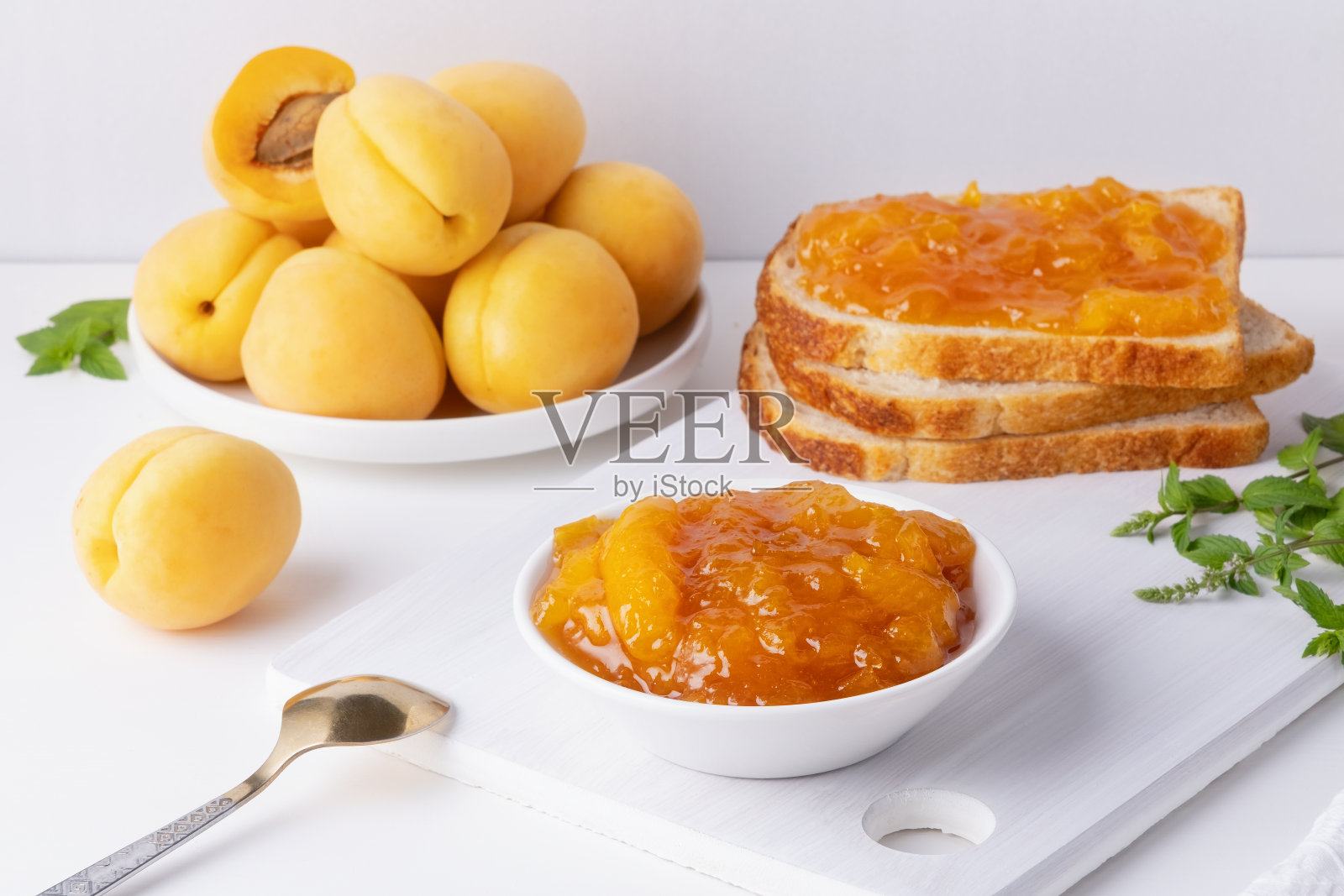 白木桌上放着烤面包、杏酱、新鲜水果和薄荷。美味的早餐照片摄影图片