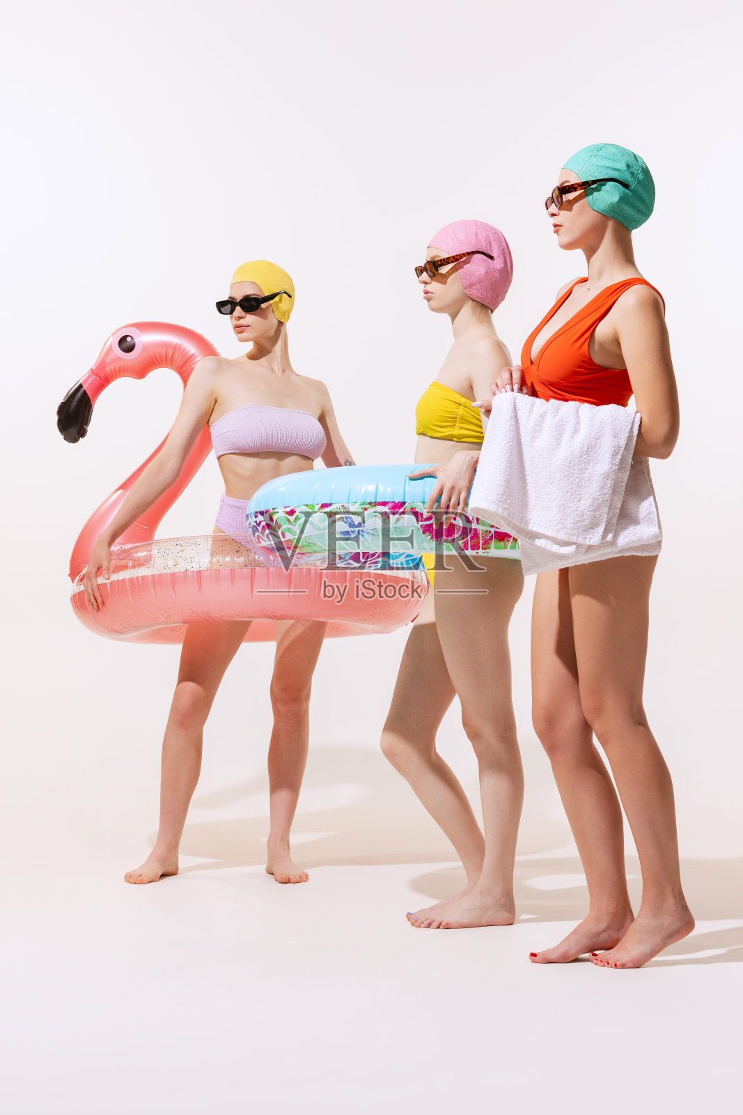 年轻女性的肖像在泳装，帽子和太阳镜与游泳圈孤立在灰色的工作室背景。海滩派对照片摄影图片