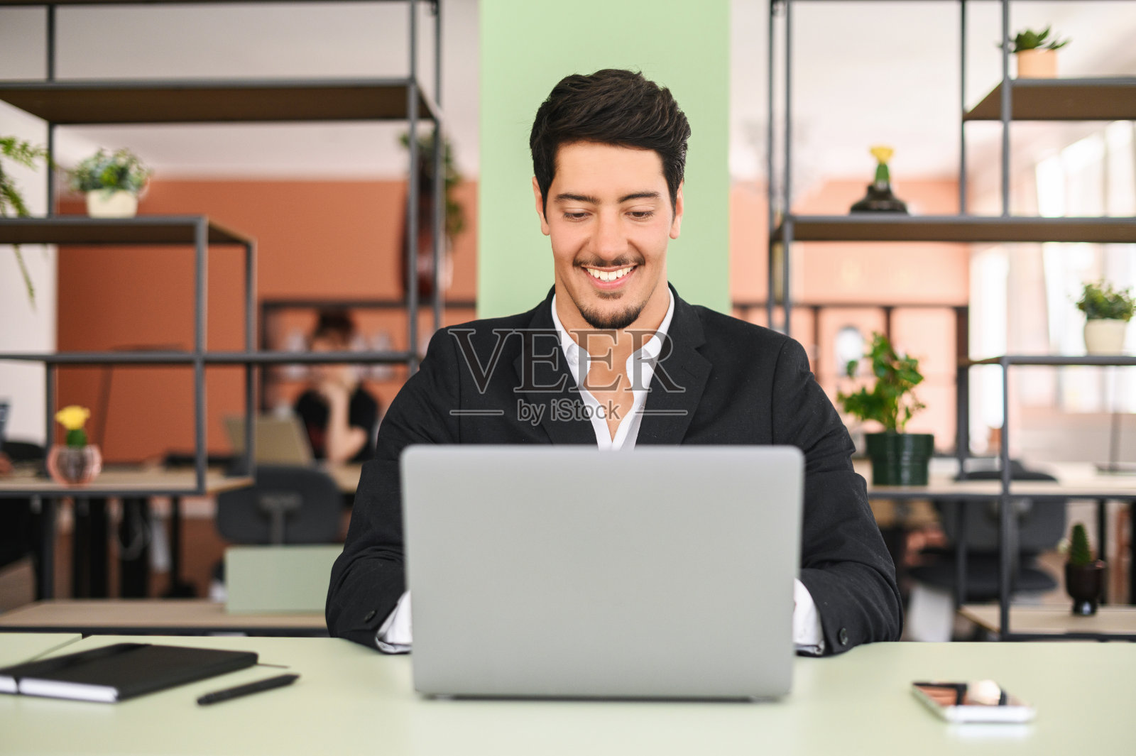 积极的拉丁黑发商人穿着正装坐在现代办公空间的办公桌前，使用笔记本电脑，进行商务通信，回复电子邮件照片摄影图片