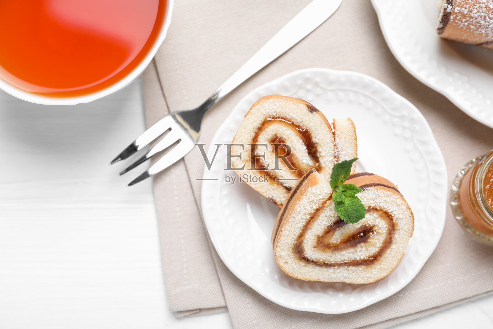 美味的果酱蛋糕卷和一杯茶放在白色的木桌上，平放着照片摄影图片
