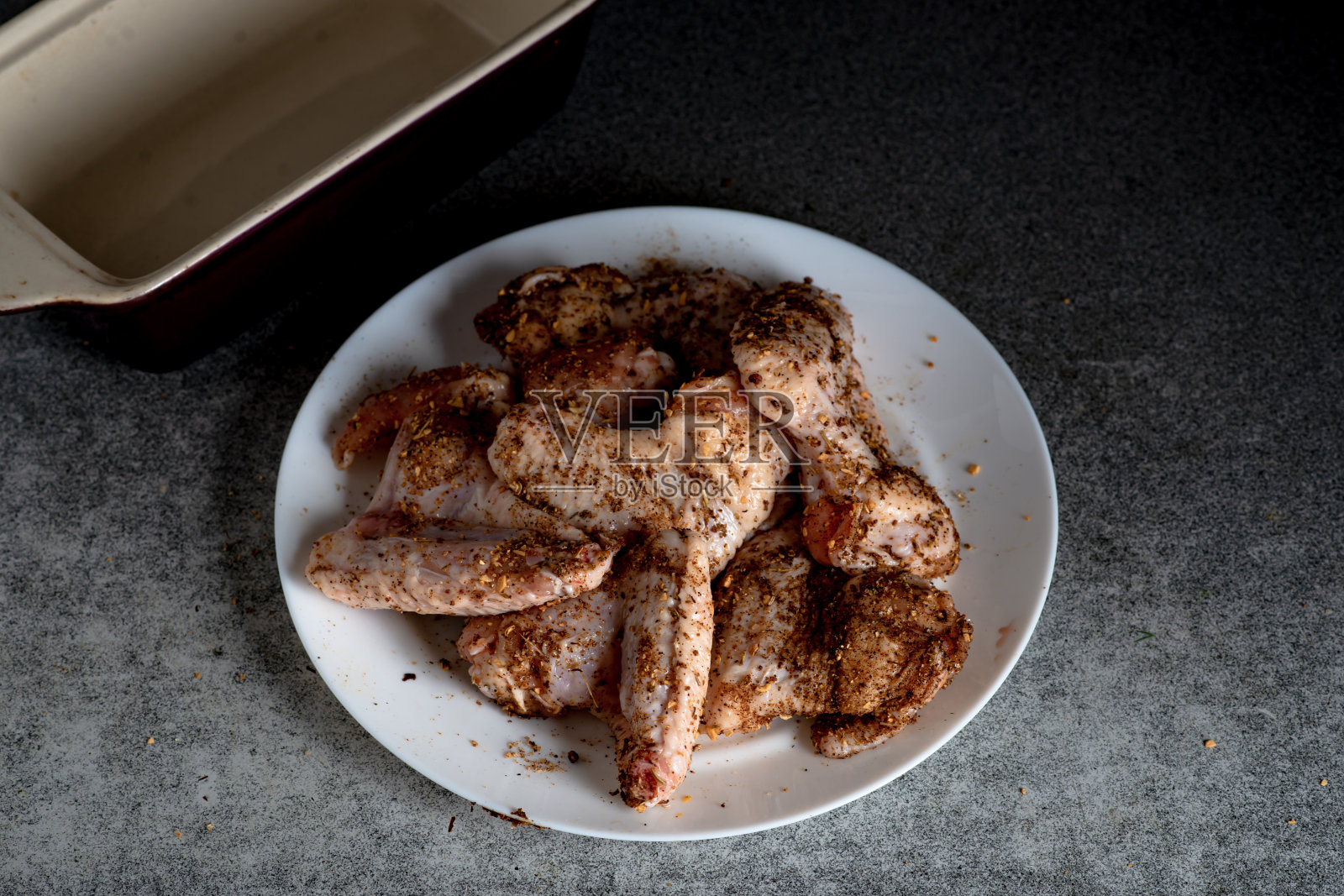 生鸡翅和香料放在厨房桌子上的白色盘子里。准备烧烤。照片摄影图片
