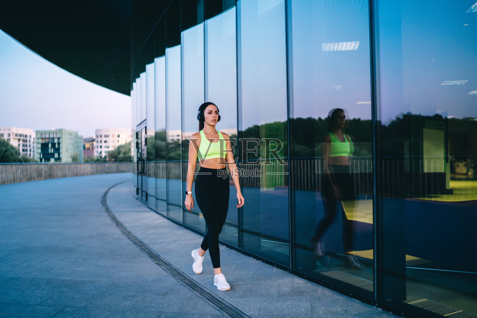 苗条的女运动员戴着耳机走在现代建筑训练后照片摄影图片