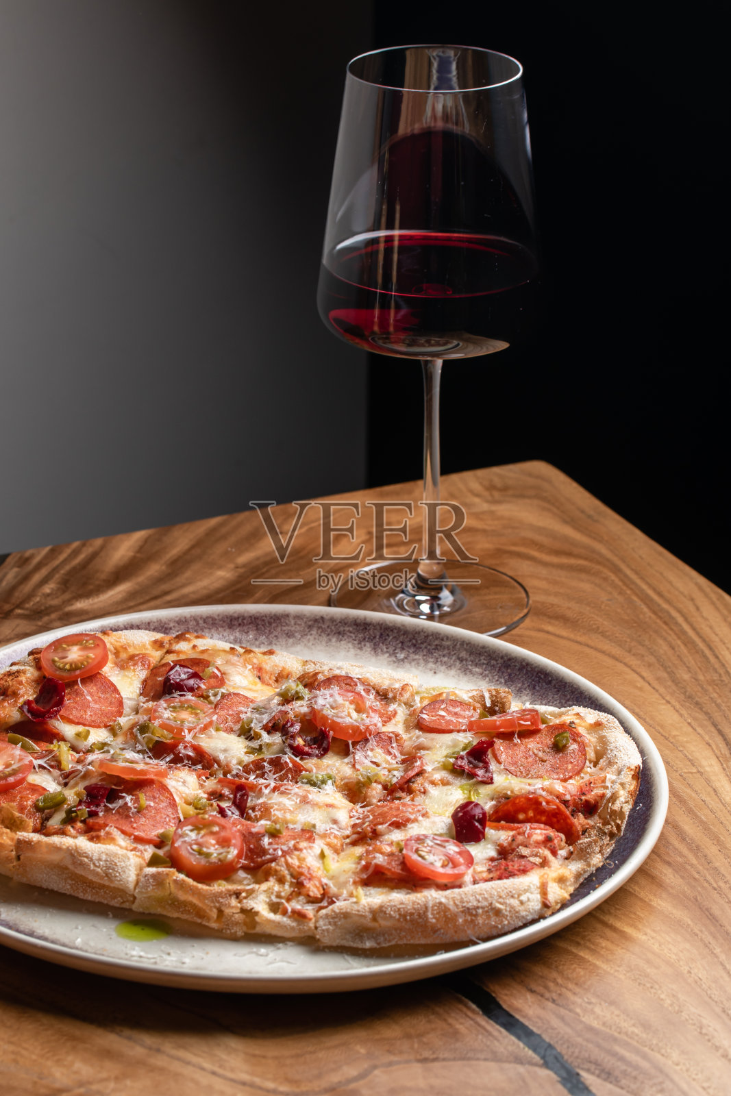 罗马披萨配意大利腊肠，圣女果和帕尔马干酪，配一杯红酒，放在木桌上照片摄影图片