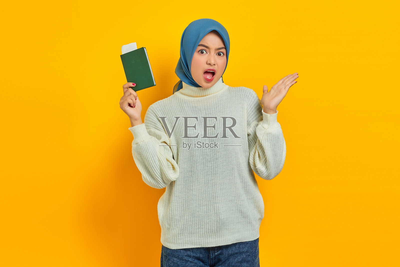 震惊美丽的亚洲女人在白色毛衣持有护照和显示复印空间的手掌孤立在黄色背景。夏天的旅行照片摄影图片