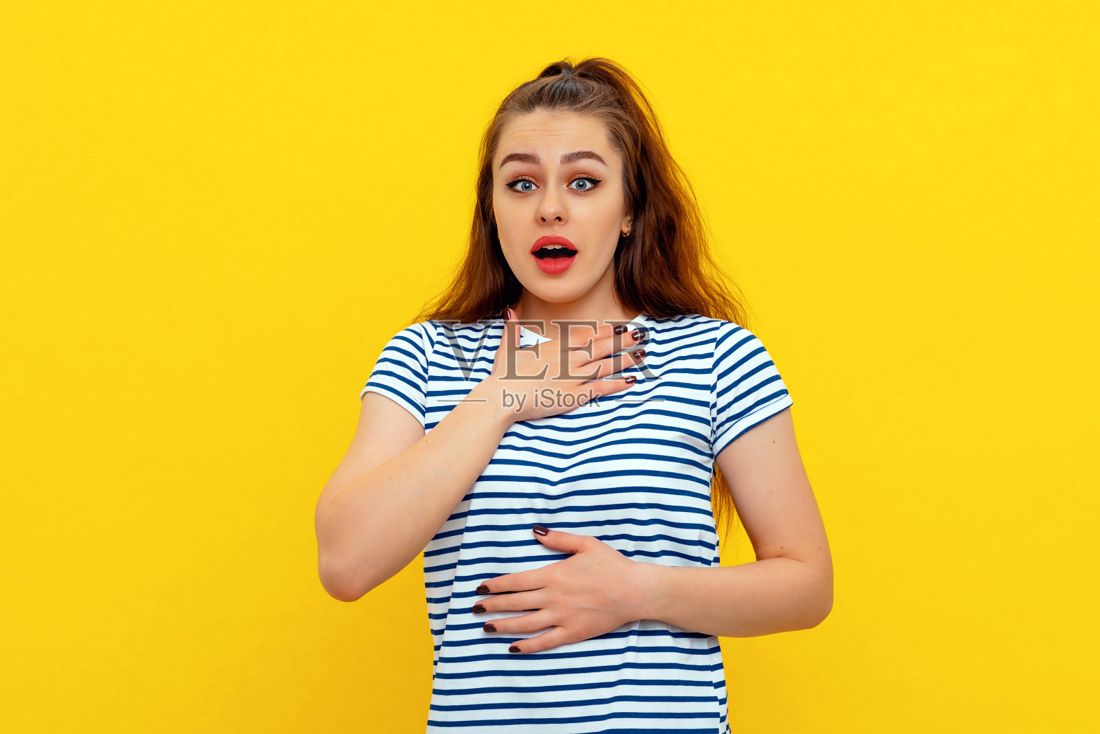 可爱的女孩在白色蓝色条纹t恤上孤立的黄色背景与震惊的表情。年轻的情绪化的女人照片摄影图片