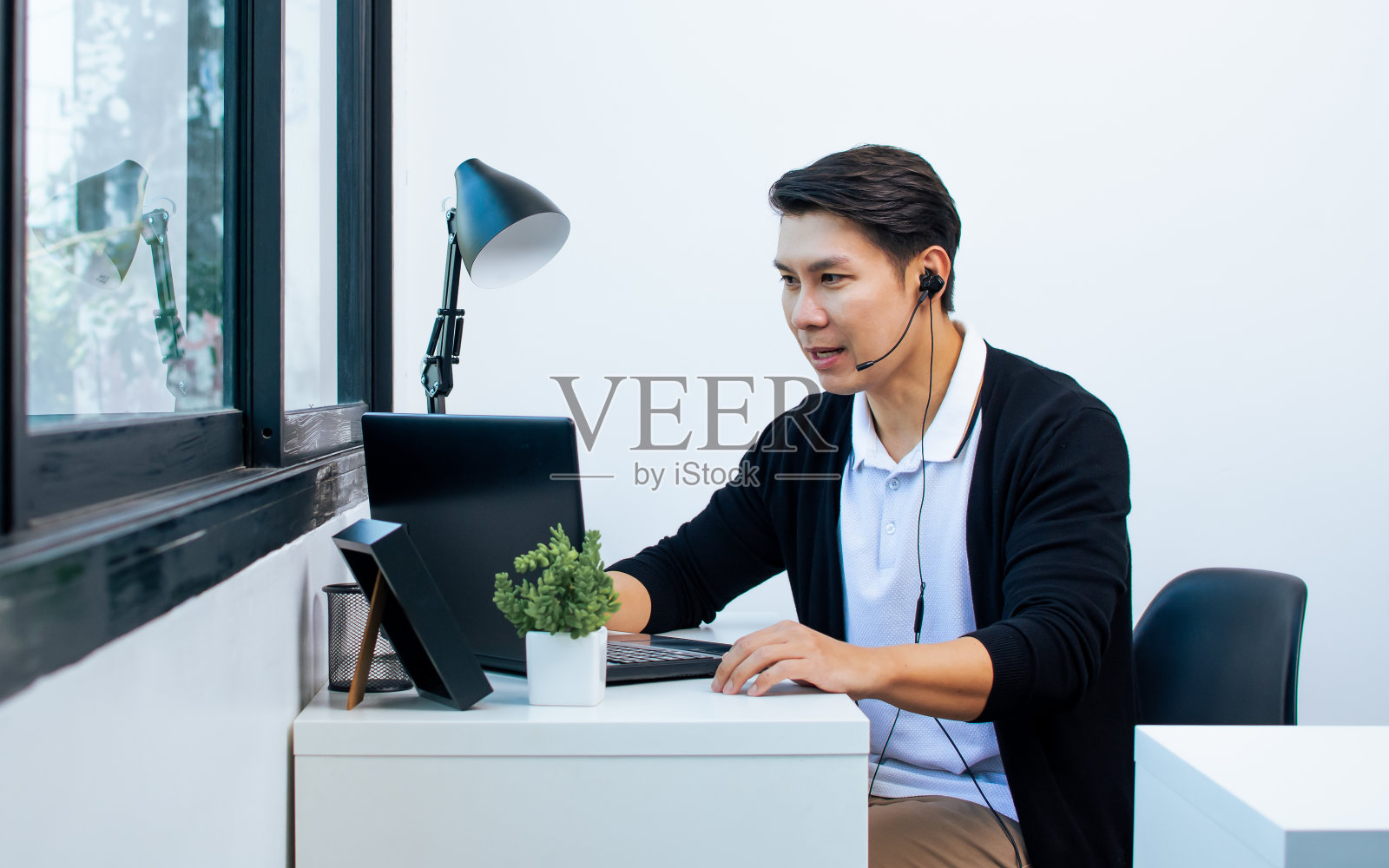 穿着休闲衬衫，戴着耳机，在家用笔记本上网学习或教学，面带积极快乐的微笑的亚洲帅哥。新常态、新科技理念。照片摄影图片