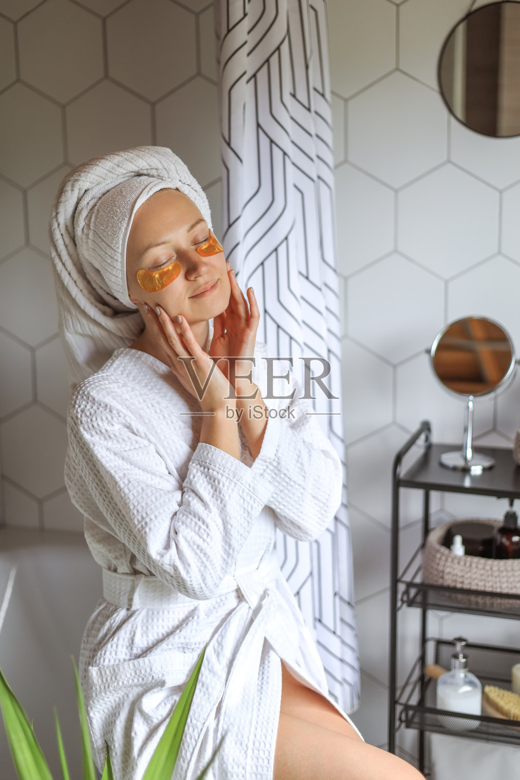 日美家居护肤。浴室内部，微笑的年轻女子淋浴后用毛巾敷在头上，用金色的眼罩保湿照片摄影图片