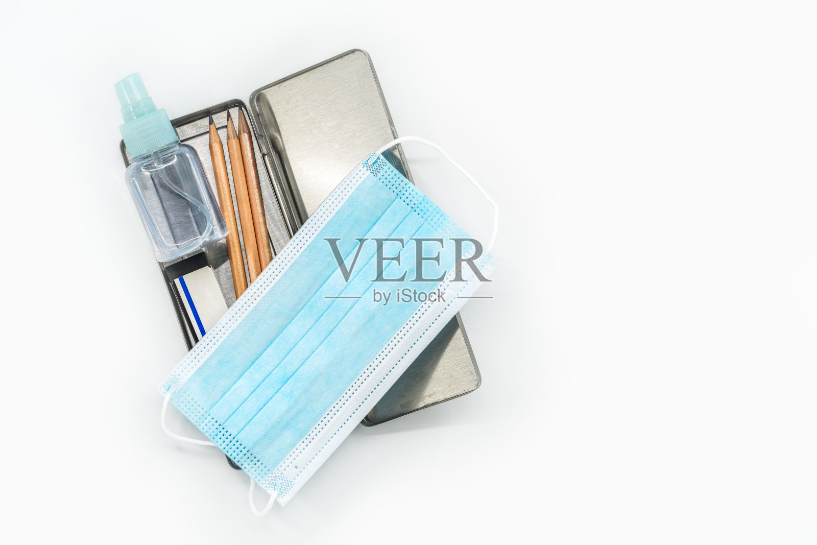 顶视图不锈钢铅笔盒，内有铅笔、医用口罩和一小瓶酒精，白色背景上的孤立图像，新冠病毒时代的返校概念。照片摄影图片